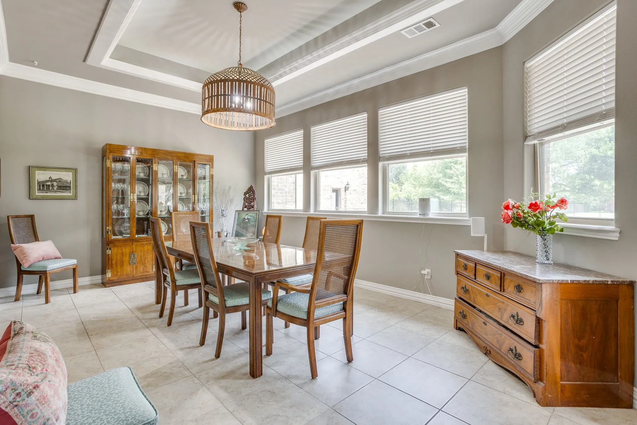 Dining area featuring an intricate tray ceiling, a distinctive woven pendant light fixture, and tile flooring