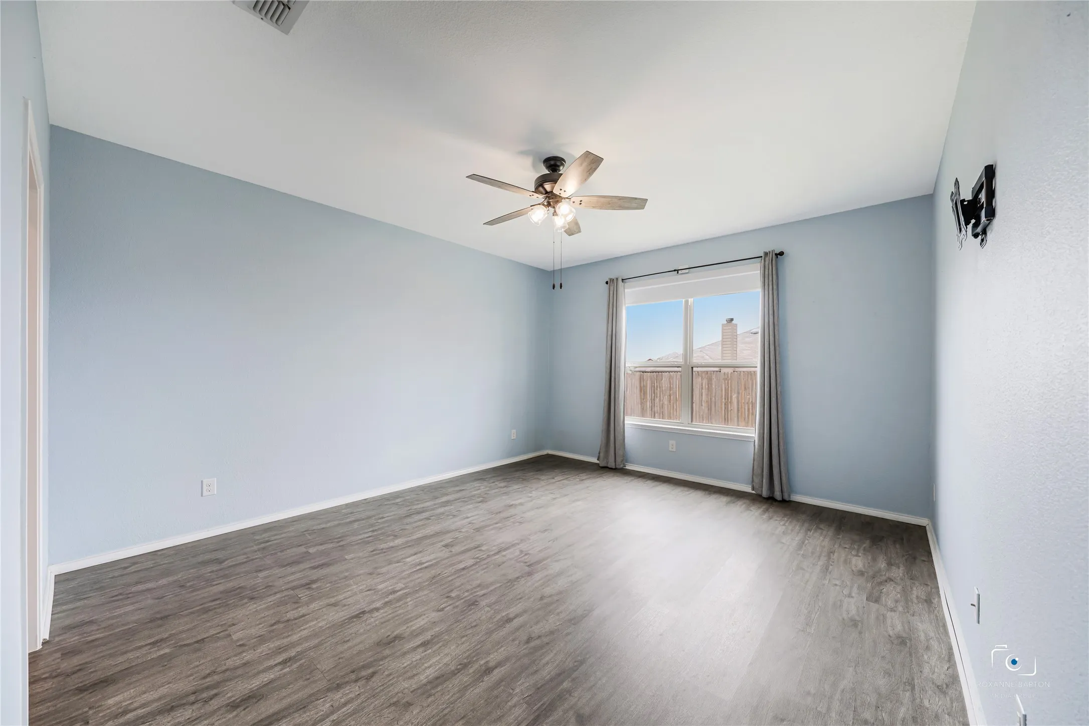 Primary suite with luxury vinyl floors and a window looking onto the large backyard. Notice the large wall space for furniture placement.