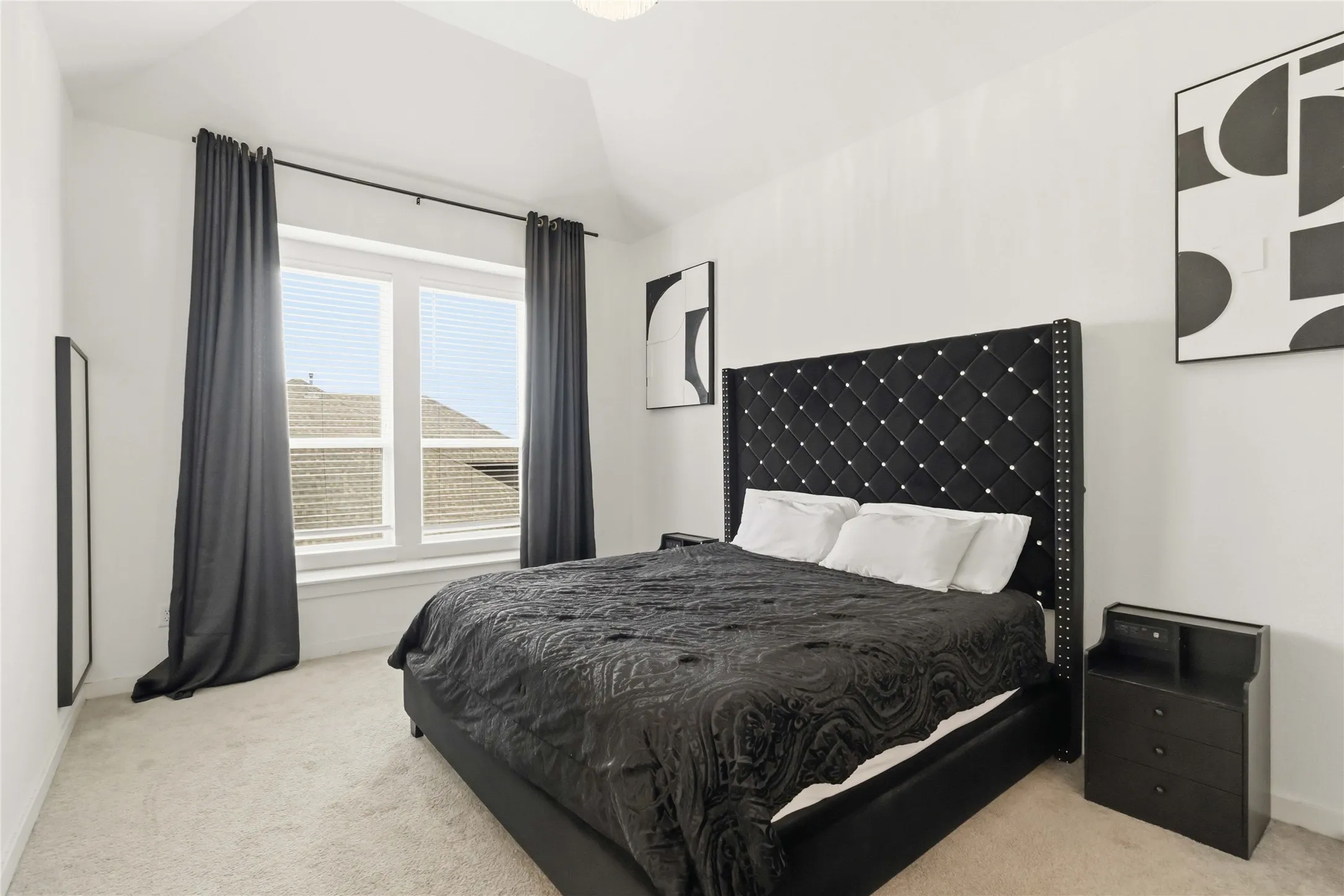 Carpeted interior space featuring a double window with blinds and dark drapery, white walls, and a vaulted ceiling