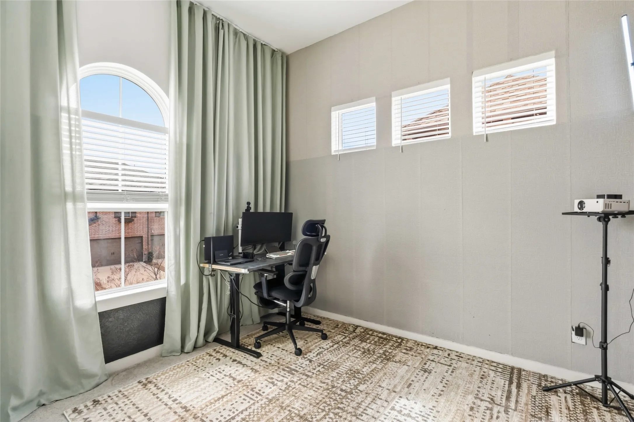 Room featuring a large arched window with blinds and floor-length drapes, three rectangular transom windows with blinds, light-toned walls, and patterned carpet flooring
