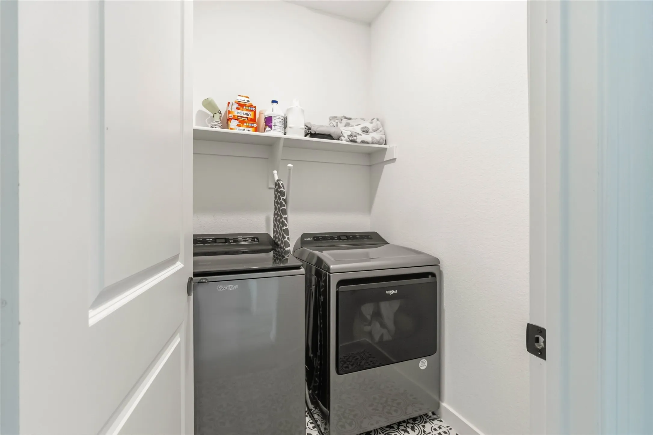 Dedicated laundry area featuring white walls, a built-in white shelf for storage, and stylish patterned floor tiling