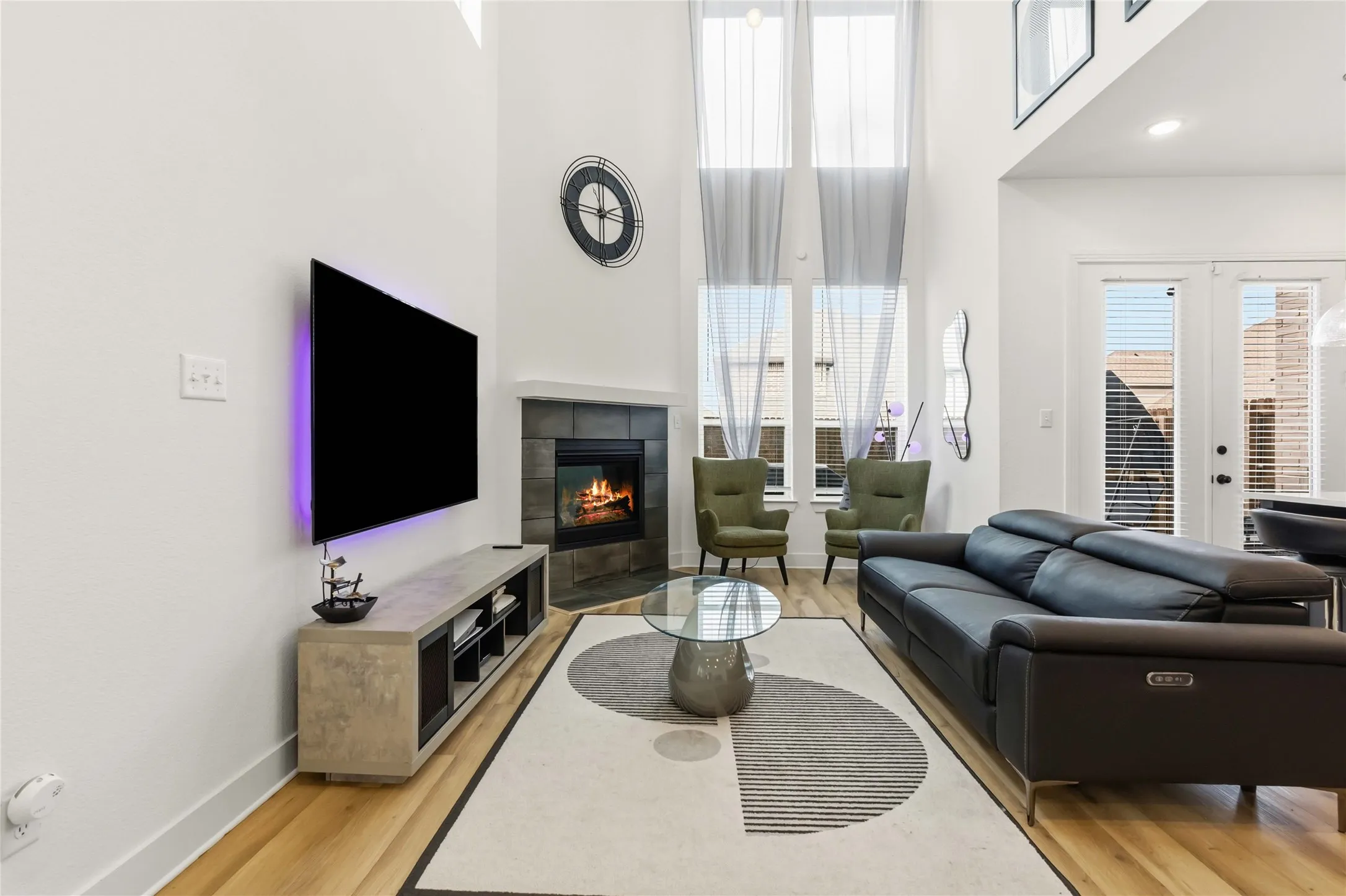 Living area featuring vaulted ceilings, wood-finish flooring, a tiled fireplace with mantel, and tall windows
