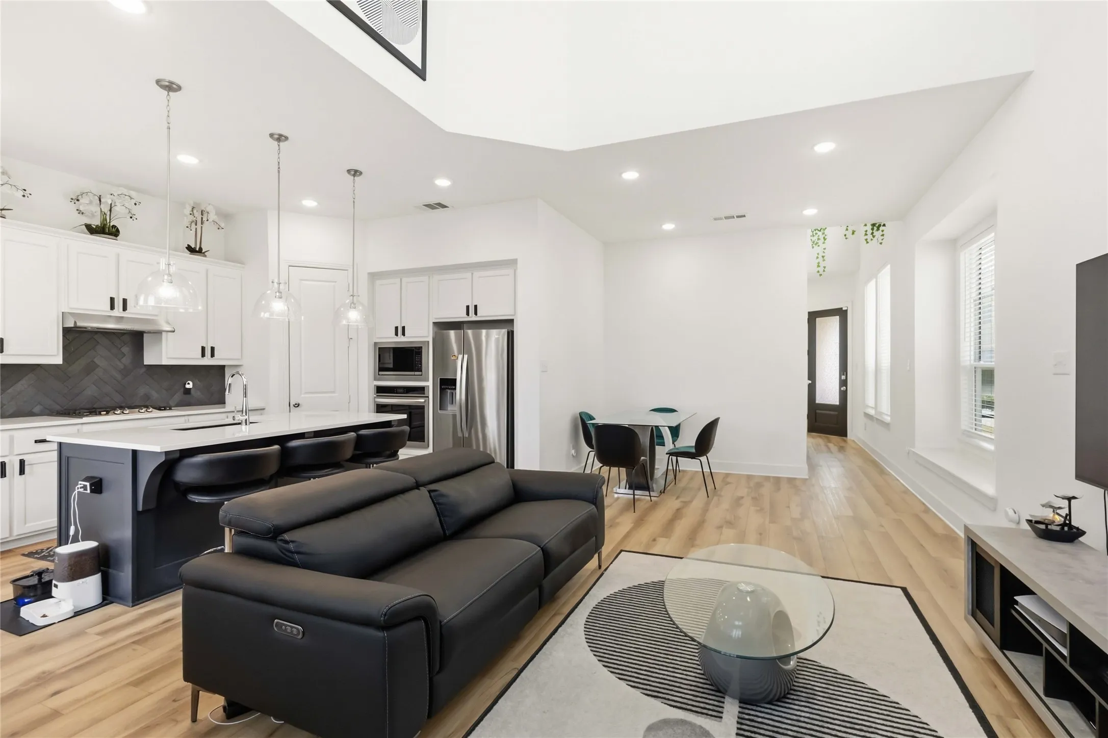 Open-concept living space featuring wood-finish flooring, recessed lighting, and a kitchen with an island, stone countertops, and stainless steel appliances