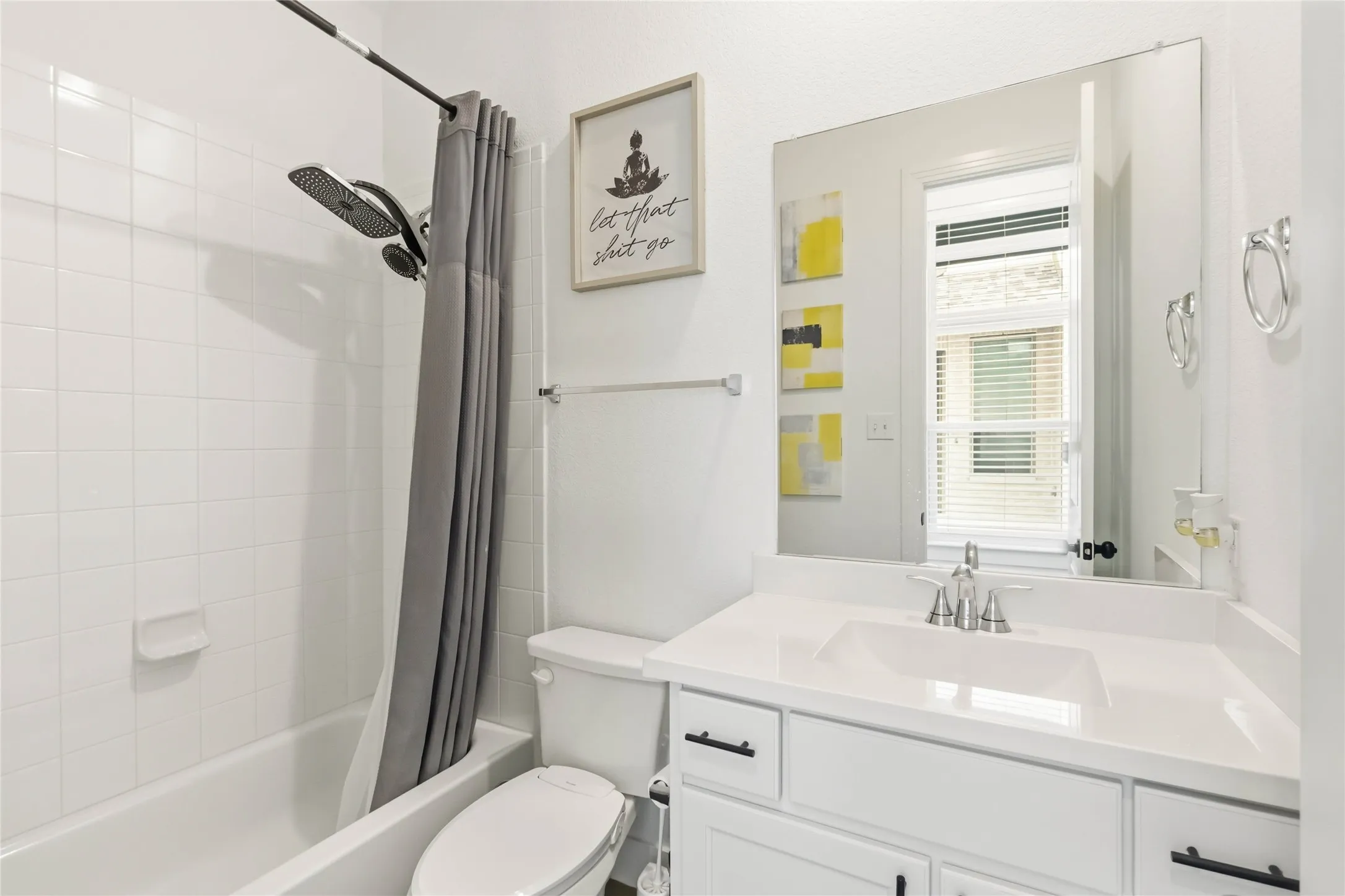 Bright bathroom featuring a white tile shower with a dual showerhead, a white vanity with an integrated sink and chrome faucet, a rectangular mirror, and a window with blinds