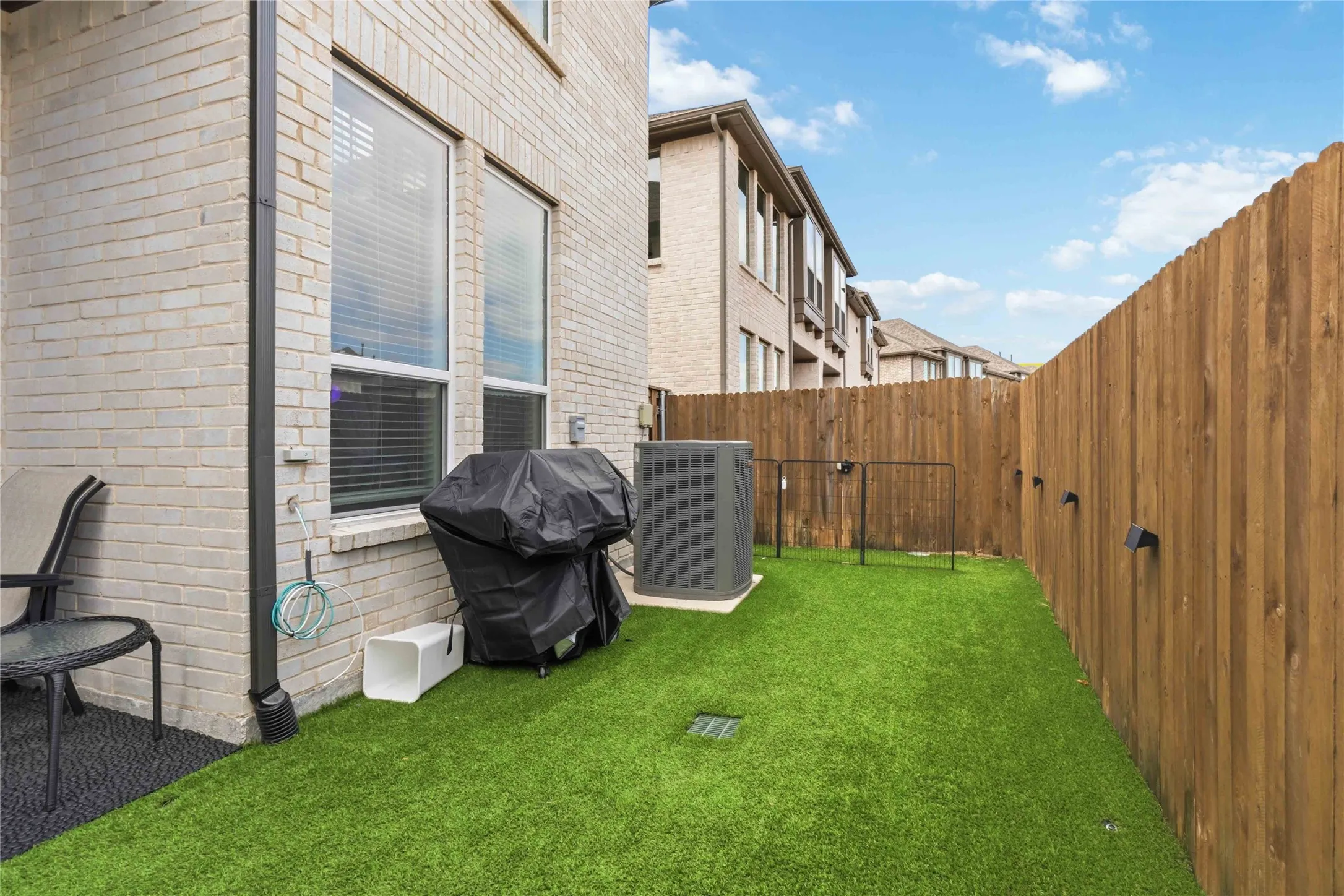 Private yard featuring artificial turf and a wood privacy fence with mounted lighting