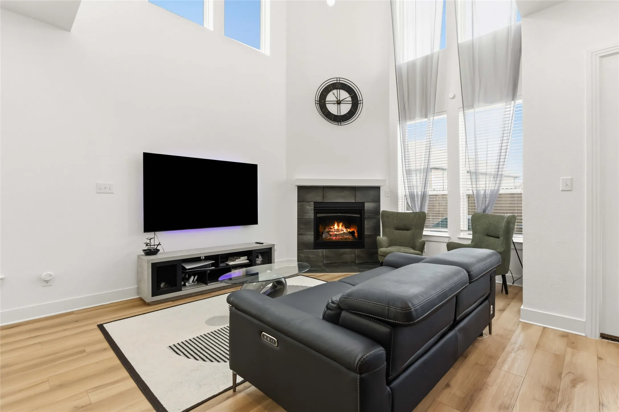 Vaulted ceilings with high windows, a fireplace with dark tile surround, and wood-finish flooring