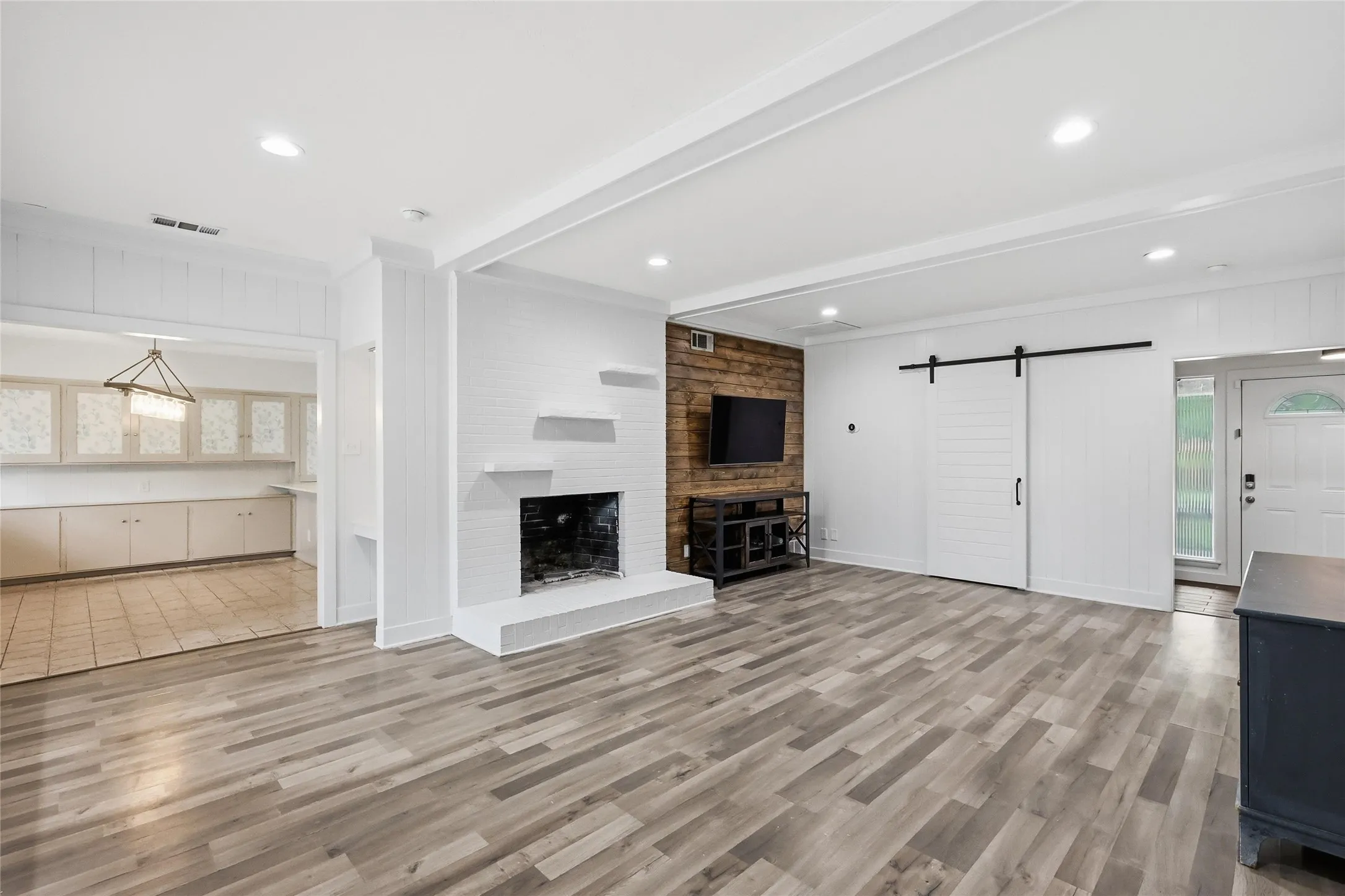 Spacious interior with wood-finish flooring, a white brick fireplace with mantel shelving, and a prominent wood-paneled accent wall