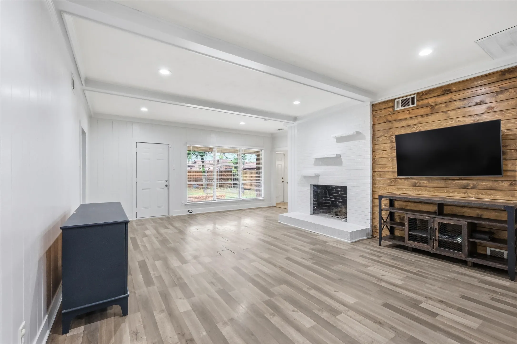 Spacious living area featuring wood-finish flooring, a white-painted brick fireplace, and a shiplap accent wall