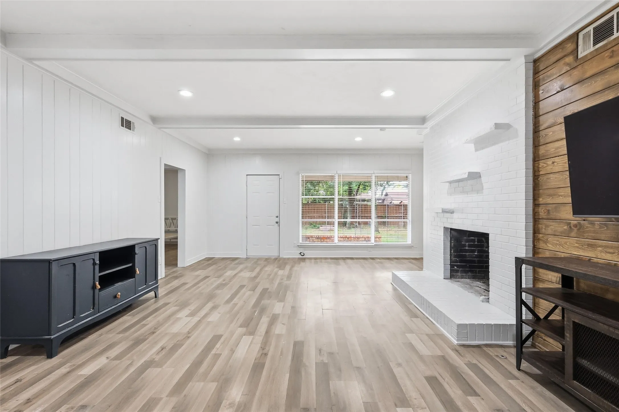 Expansive living area featuring light wood-finish flooring, a white-painted brick fireplace with a black firebox, and recessed lighting