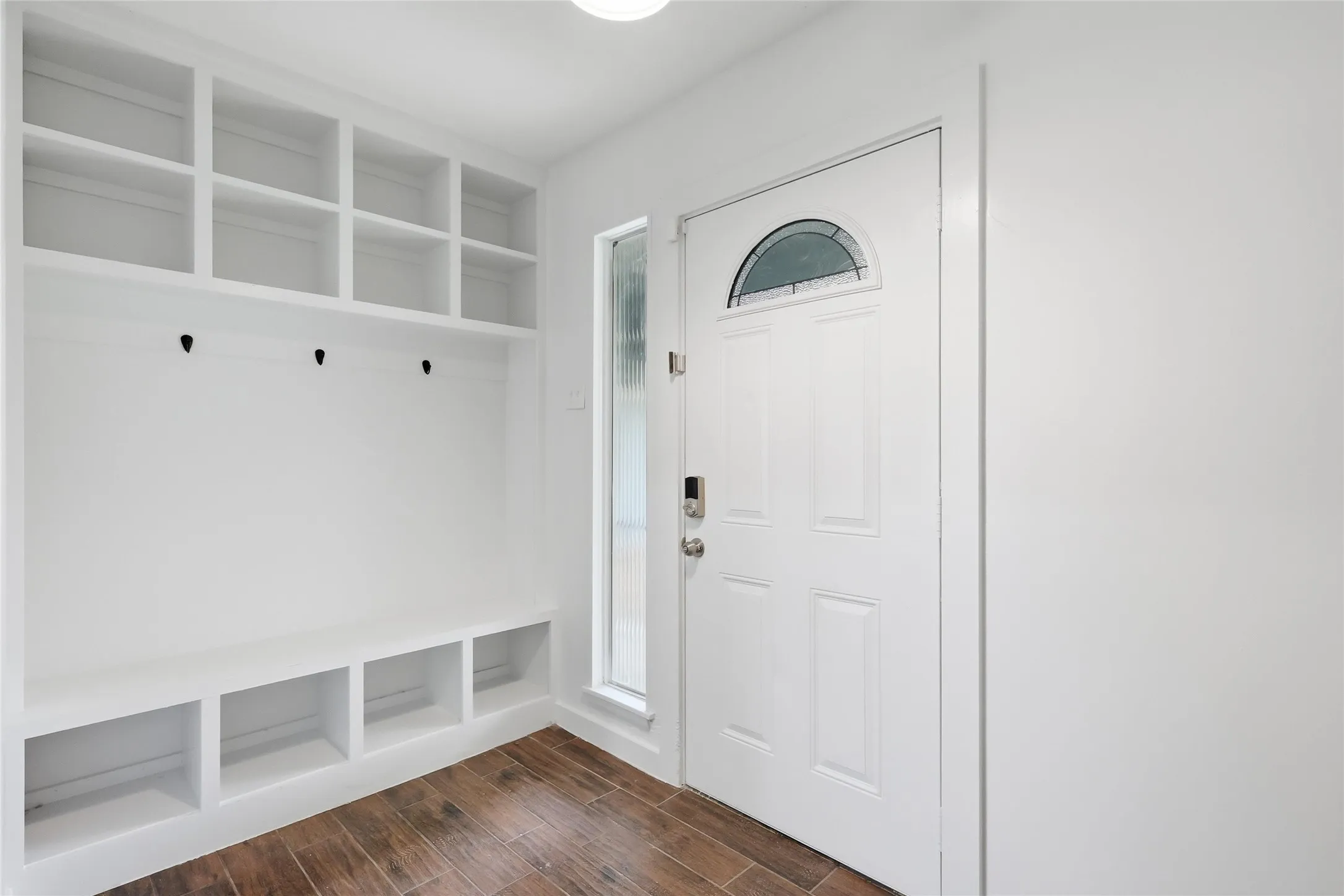 Entryway featuring wood-finish flooring, a white paneled door with an arched glass insert, a full-length sidelight, and a built-in storage unit with cubbies and hooks