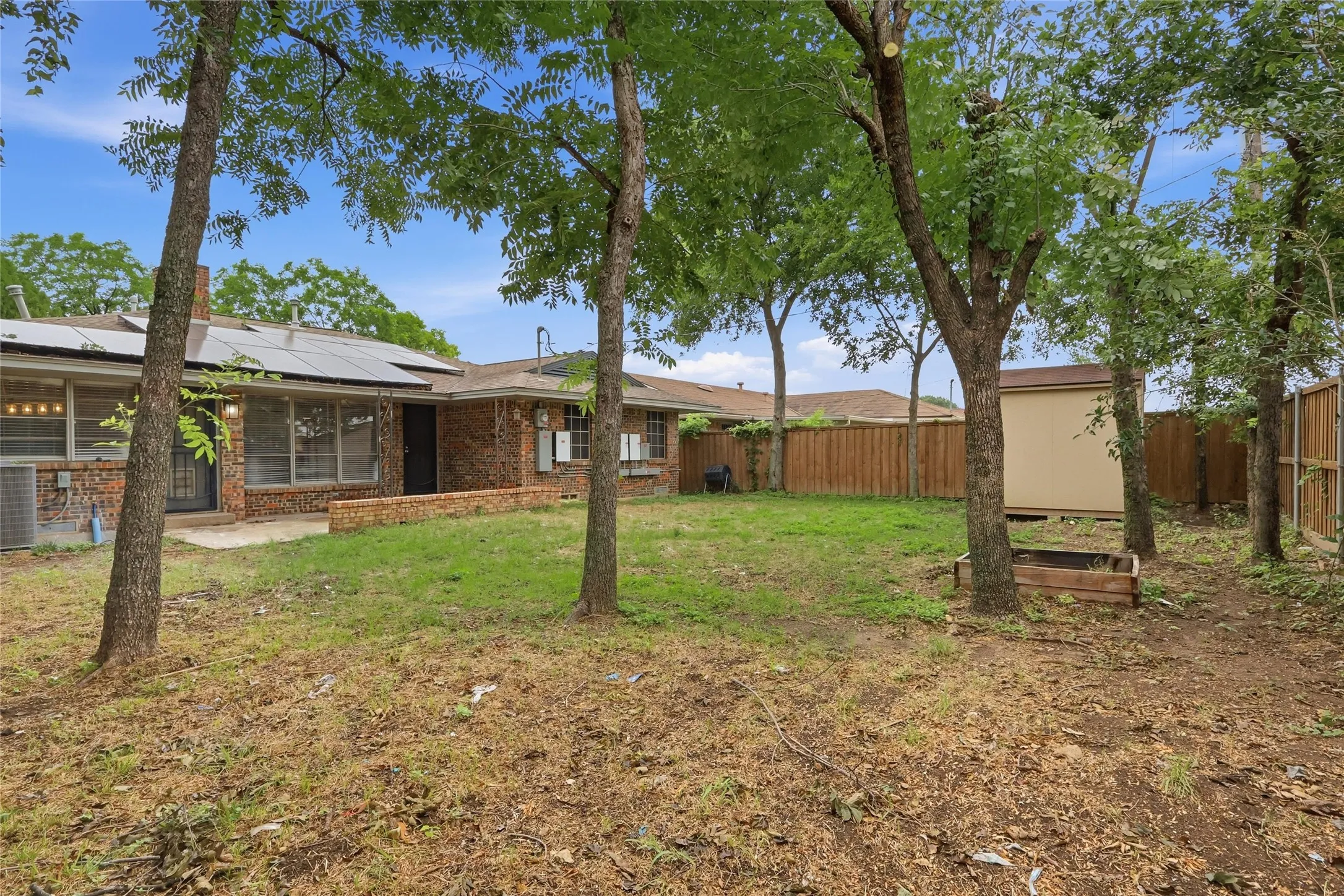 Expansive backyard featuring mature trees, a wooden privacy fence, a storage shed, and a raised garden bed