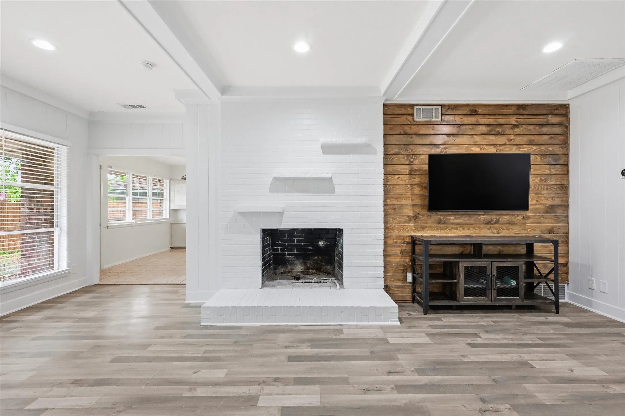 Spacious room featuring a white brick fireplace with floating mantels, a wood-panel accent wall, and wood-finish flooring