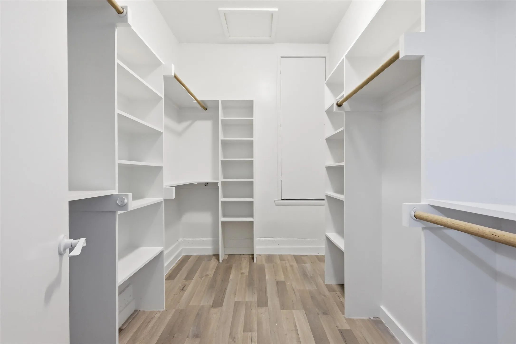 Walk-in closet featuring extensive built-in shelving, multiple hanging rods, wood-finish flooring, and a window for natural light