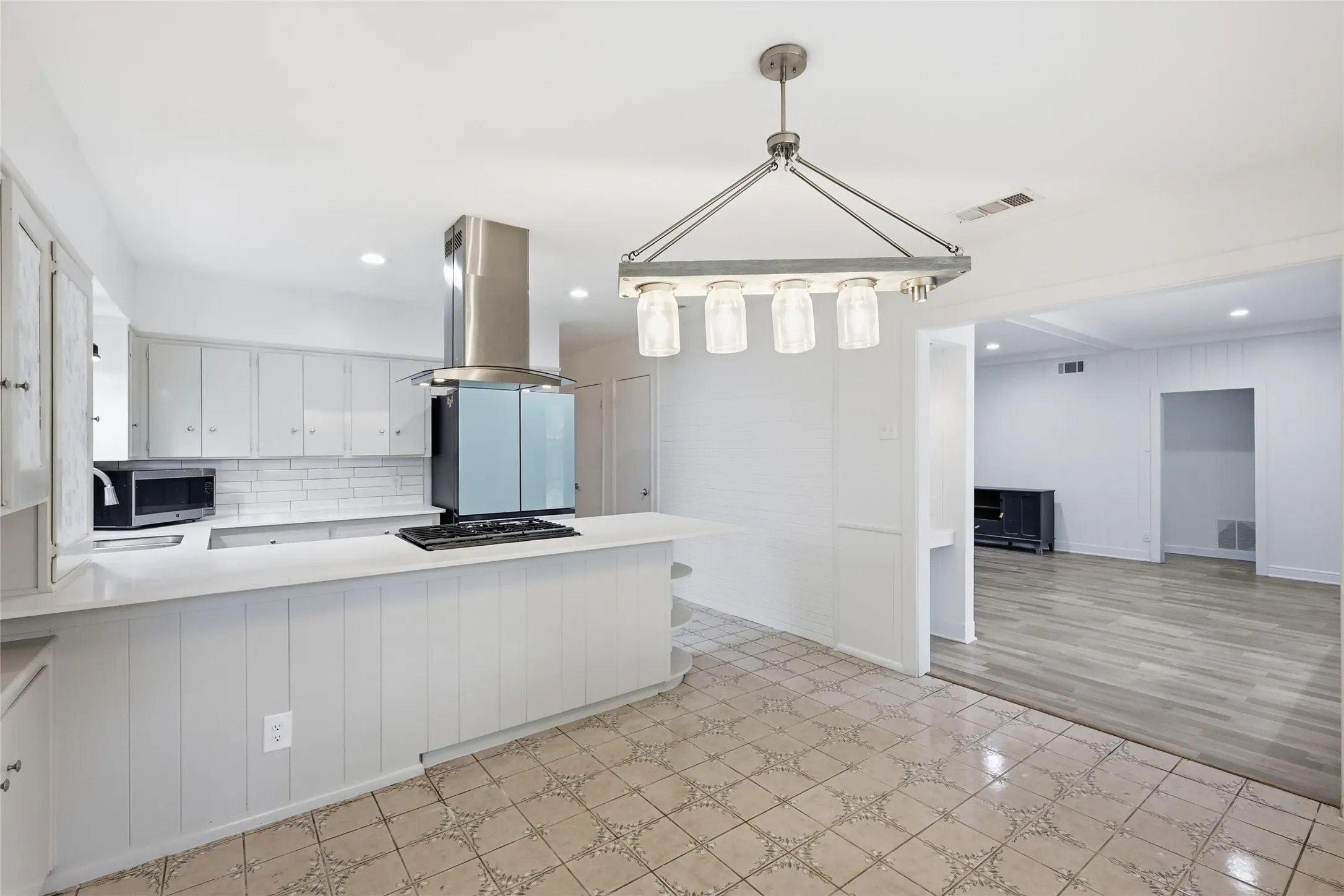Spacious kitchen featuring white cabinetry, subway tile backsplash, a stainless steel range hood, a built-in microwave, and a gas cooktop on the island