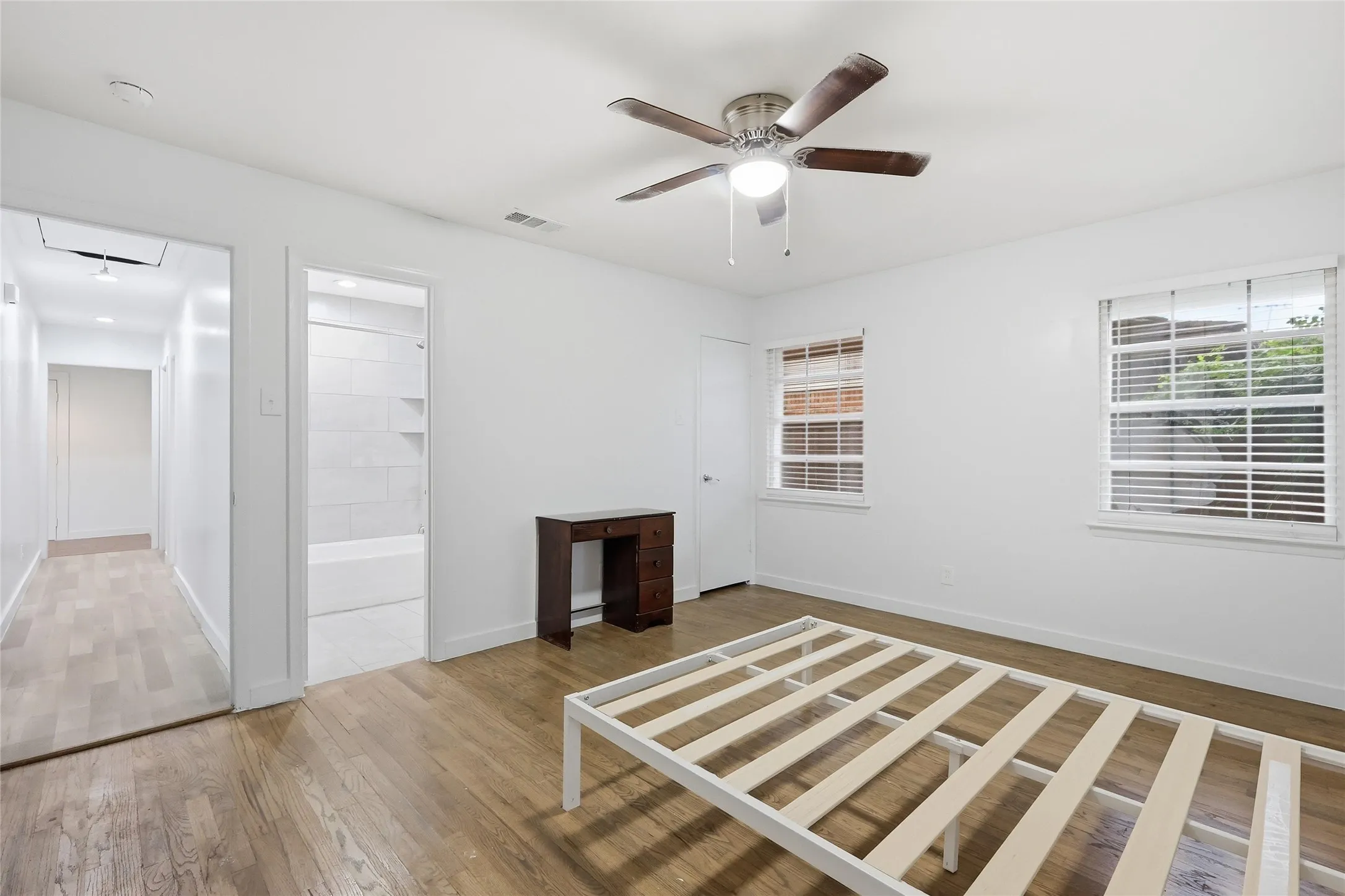 Bright room featuring wood-finish flooring, a ceiling fan with light, and two windows with blinds