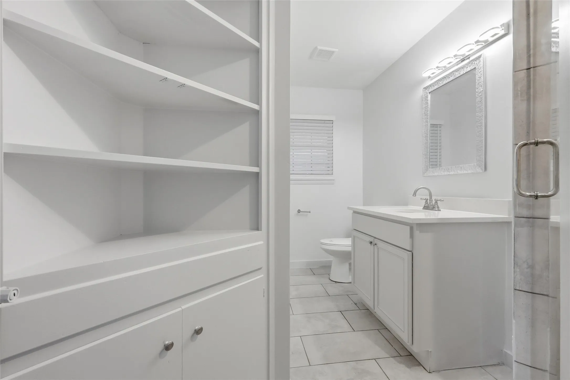 Built-in shelving and cabinetry complement a modern bathroom featuring a white vanity with integrated sink, a framed mirror, and horizontal light fixture