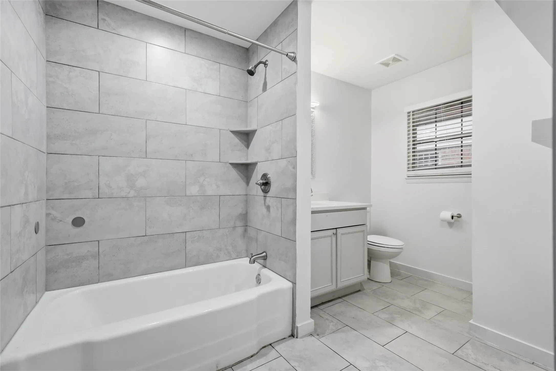 Bathroom featuring a bathtub with subway tile surround, two built-in corner shelves, and a brushed nickel showerhead