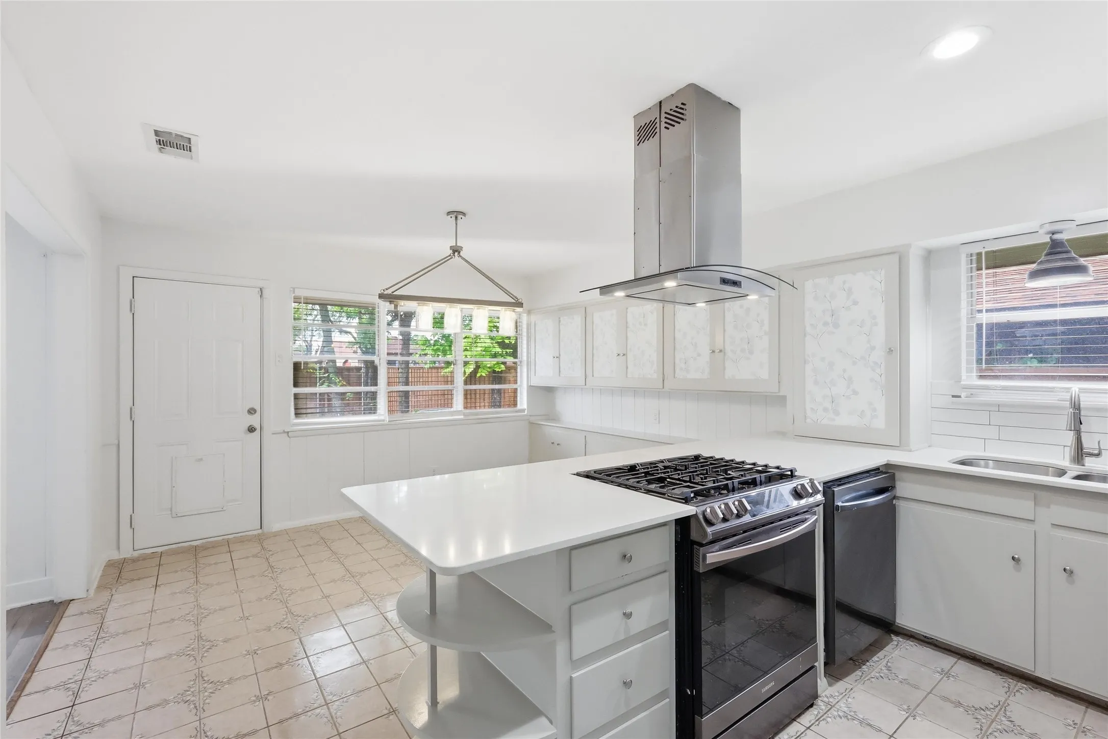 Kitchen featuring a gas range with a stainless steel range hood, quartz countertops, subway tile backsplash, and light-toned cabinetry