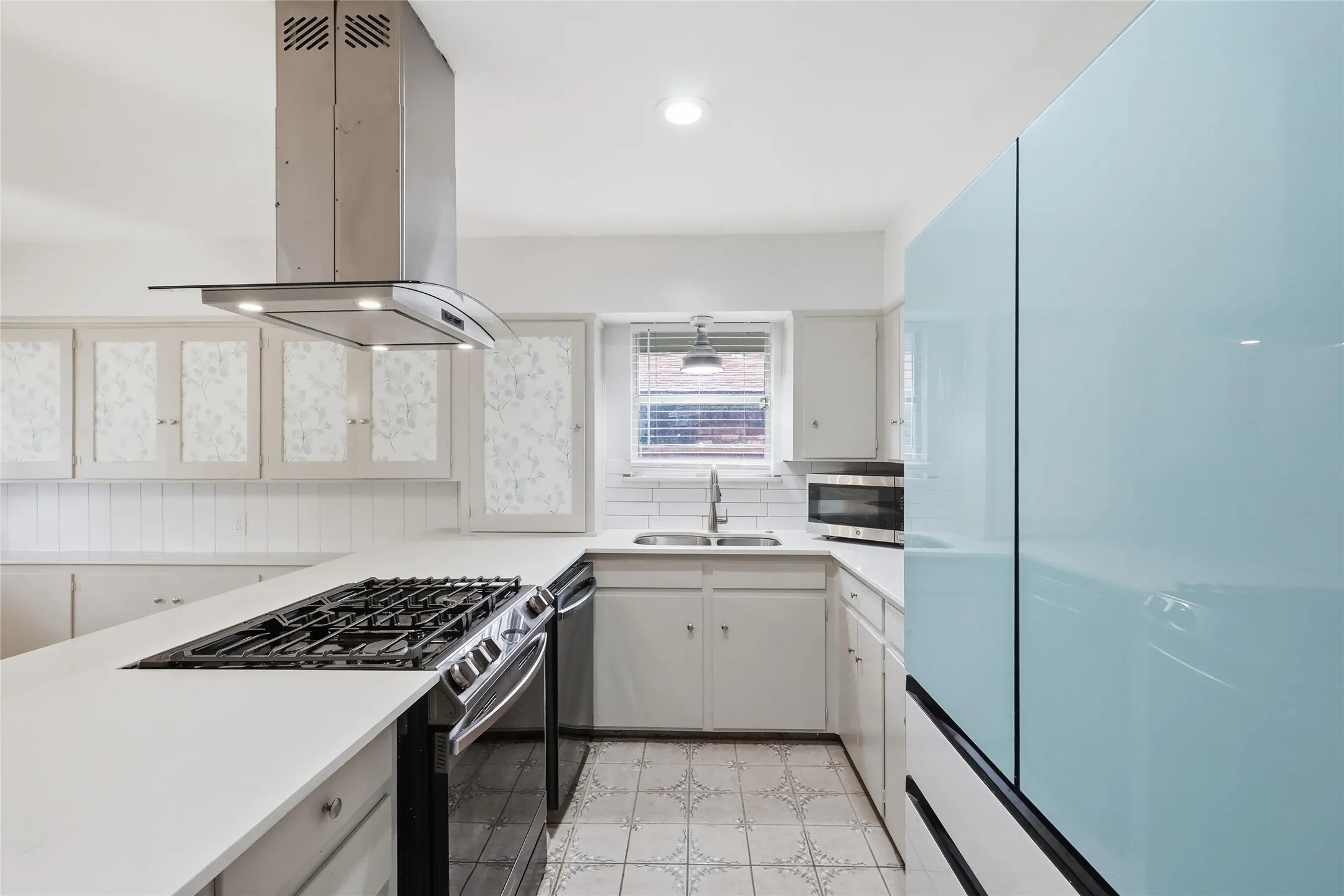 Kitchen featuring a stainless steel range with a ventilation hood, white countertops, white cabinetry, a double basin sink, and patterned floor tiles