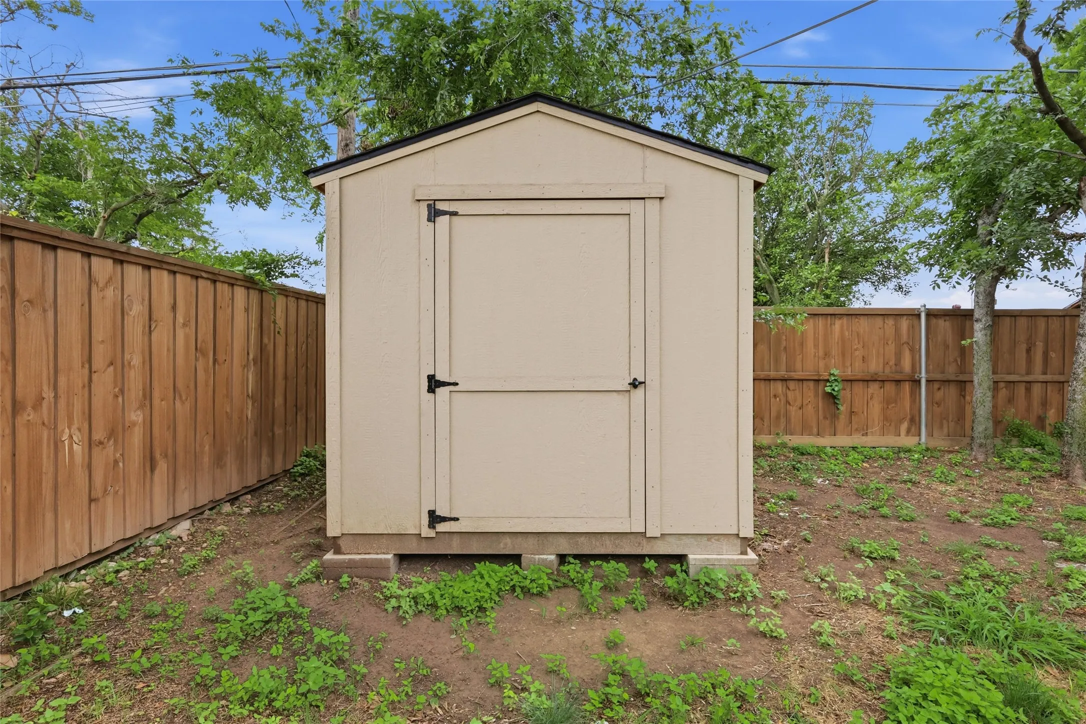 Freestanding utility shed with a tan exterior and black trim, featuring a single access door with black hardware