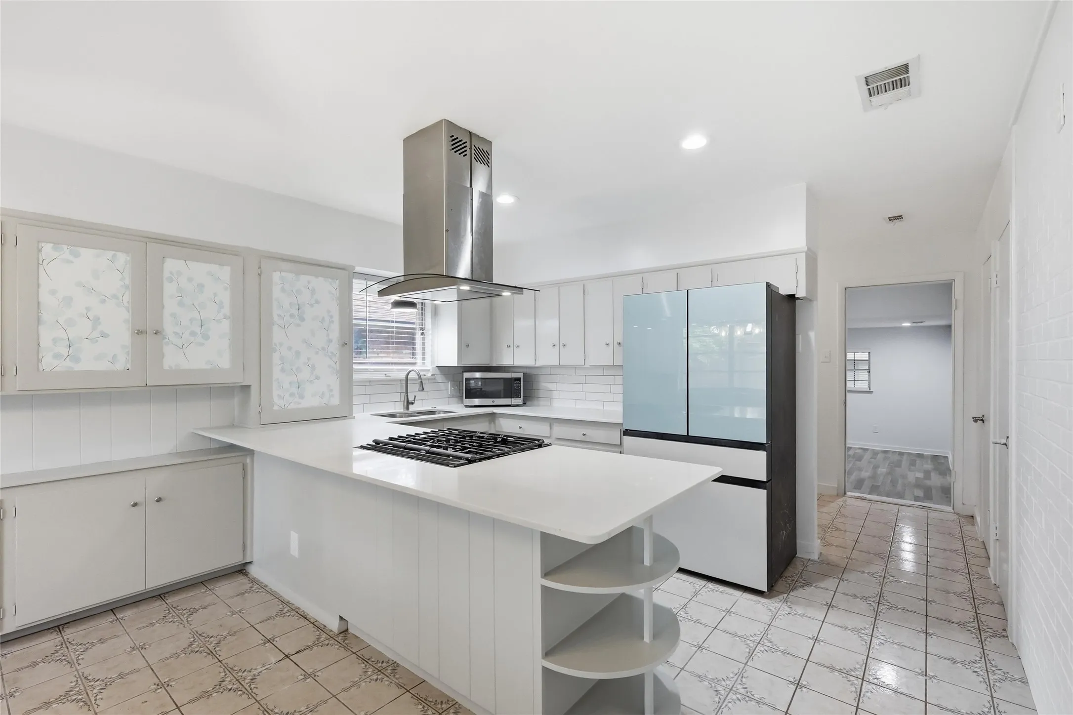 Kitchen featuring a central island with an integrated gas cooktop, a stainless steel range hood, white cabinetry, and white subway tile backsplash