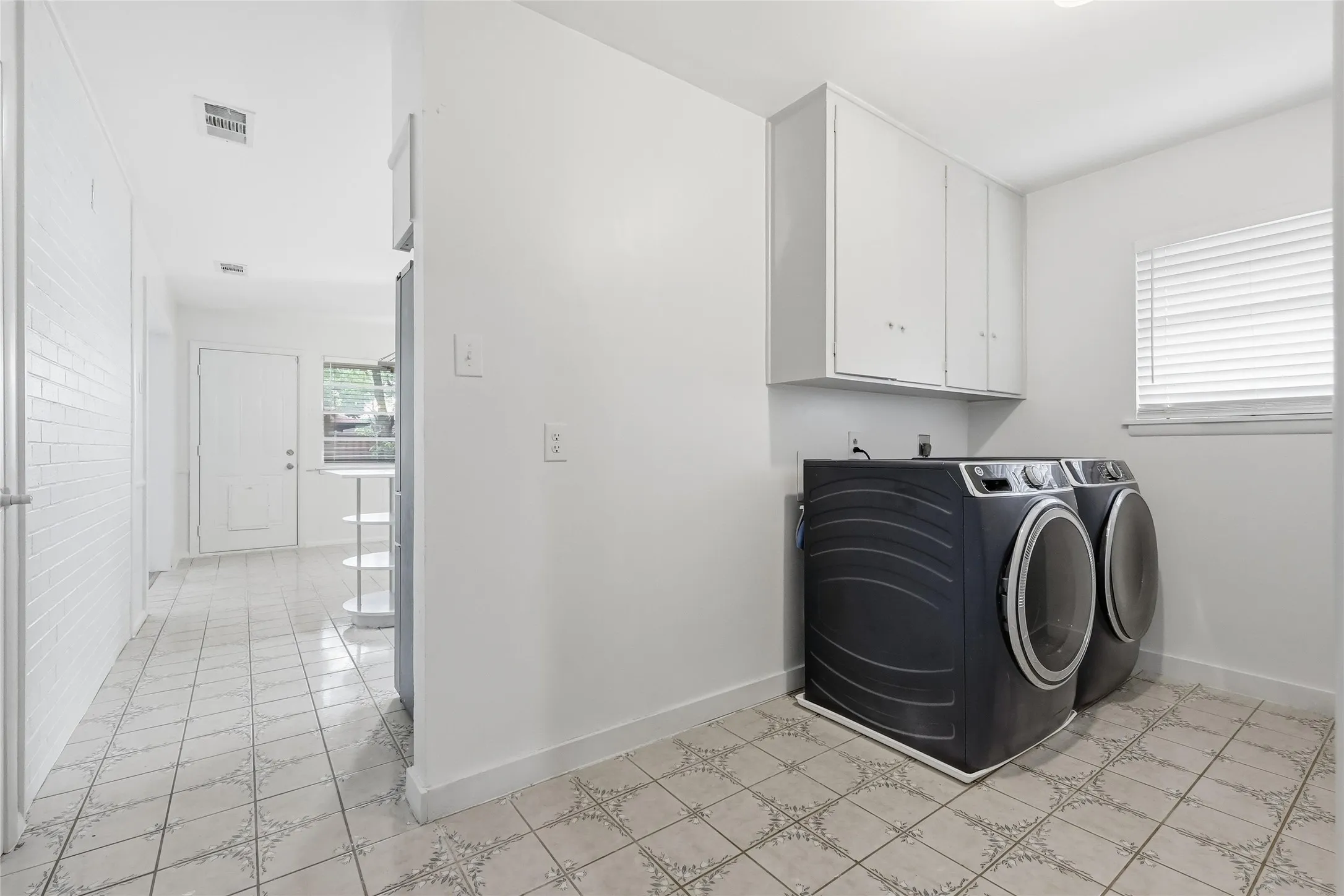 Utility area featuring white-painted walls, a window with horizontal blinds, and overhead cabinetry