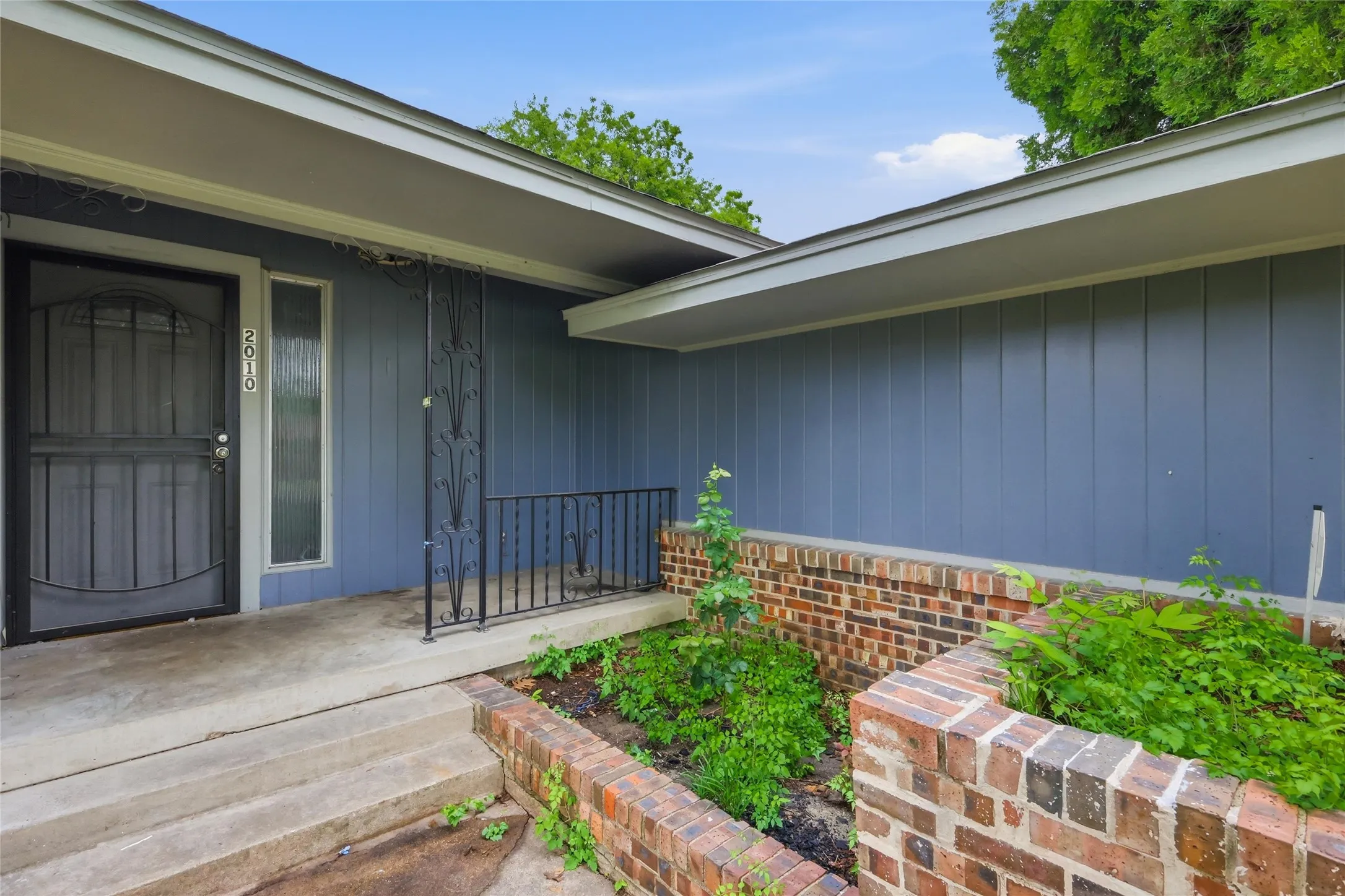 Front entry with concrete porch, brick planter beds, and board and batten siding