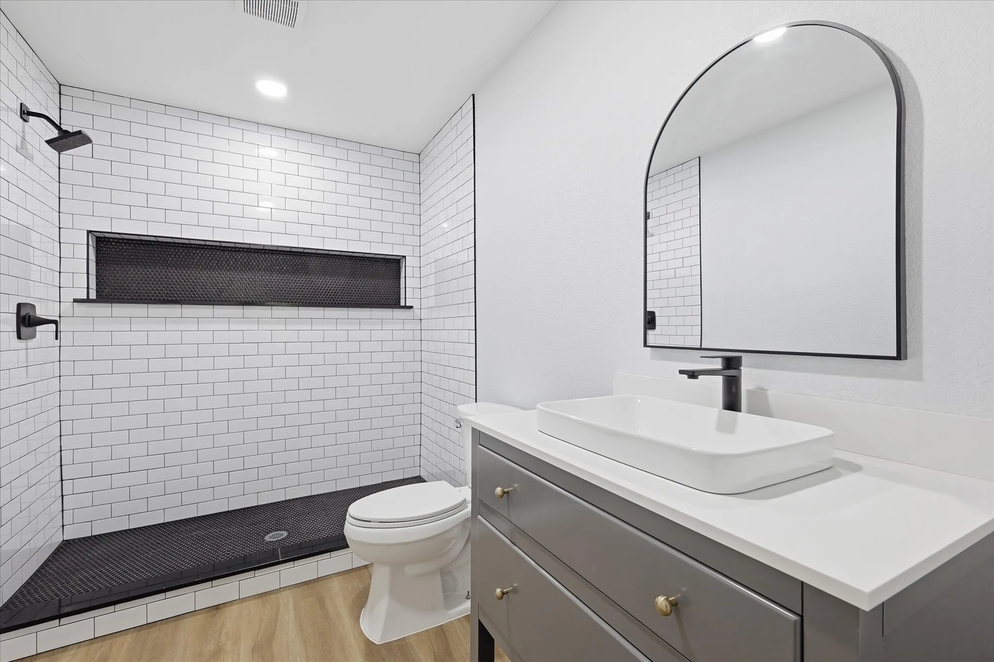Bathroom featuring a subway-tiled shower with black grout, a recessed niche, and a dark-toned shower pan