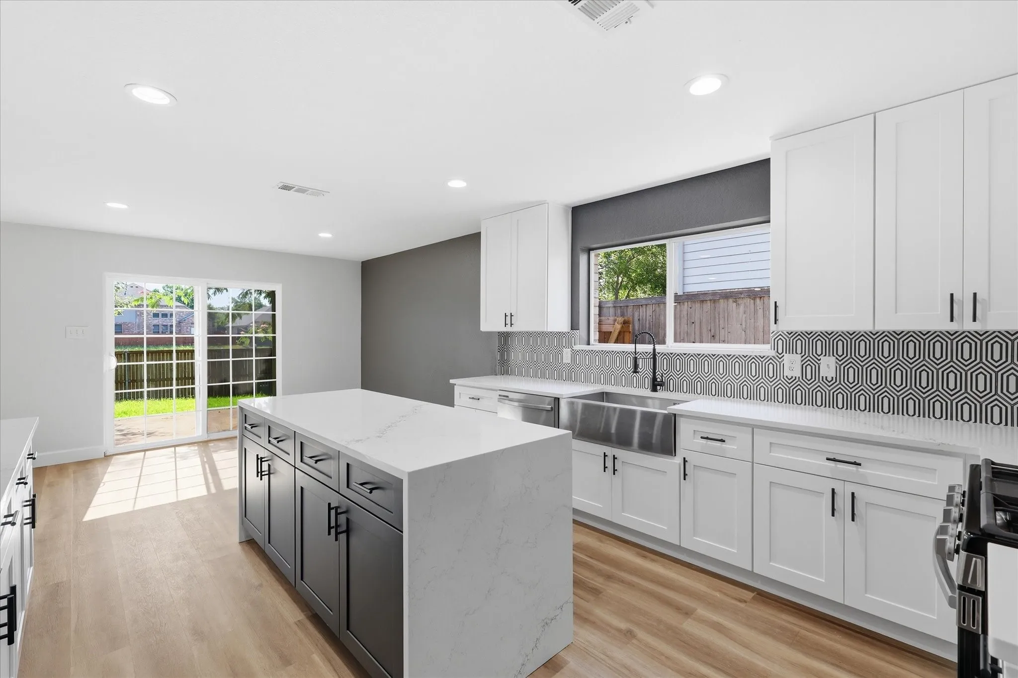 Modern kitchen featuring a waterfall island with a quartz countertop, white shaker cabinetry, a geometric tile backsplash, and wood-finish flooring