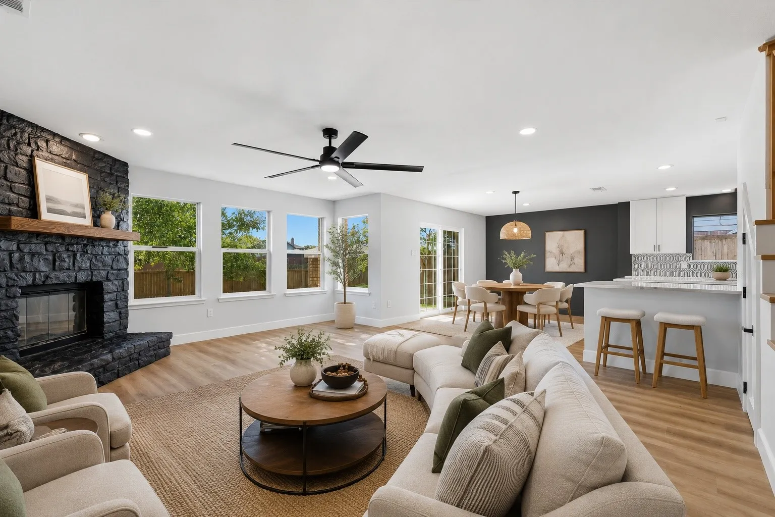 VIRTUALLY STAGED Open-concept living area featuring wood-finish flooring, a stone-faced fireplace with a substantial wood mantel, a multi-pane window line, recessed lighting, and a contemporary ceiling fan