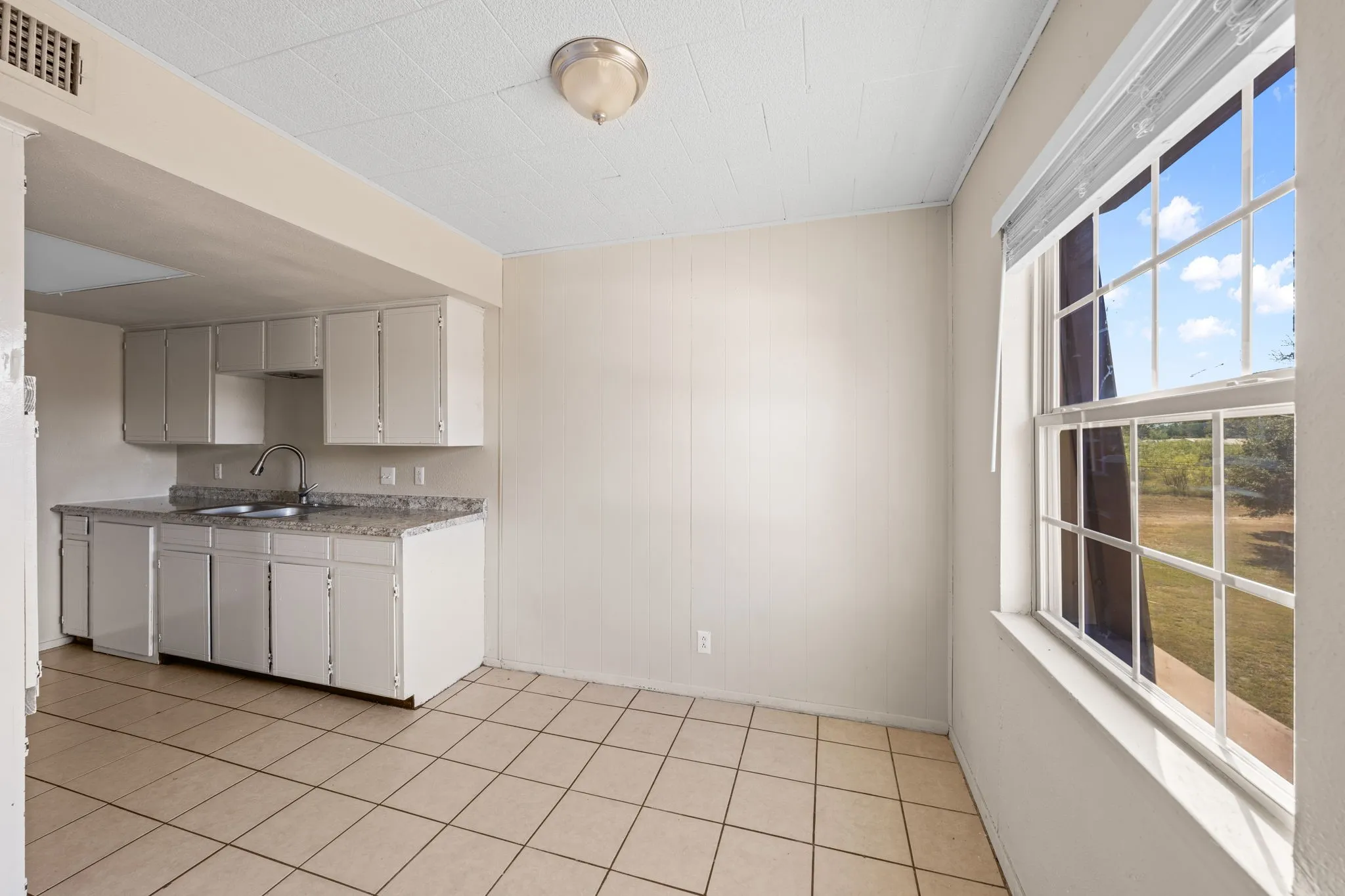 Kitchen featuring white cabinetry, wooden walls, and light tile patterned flooring