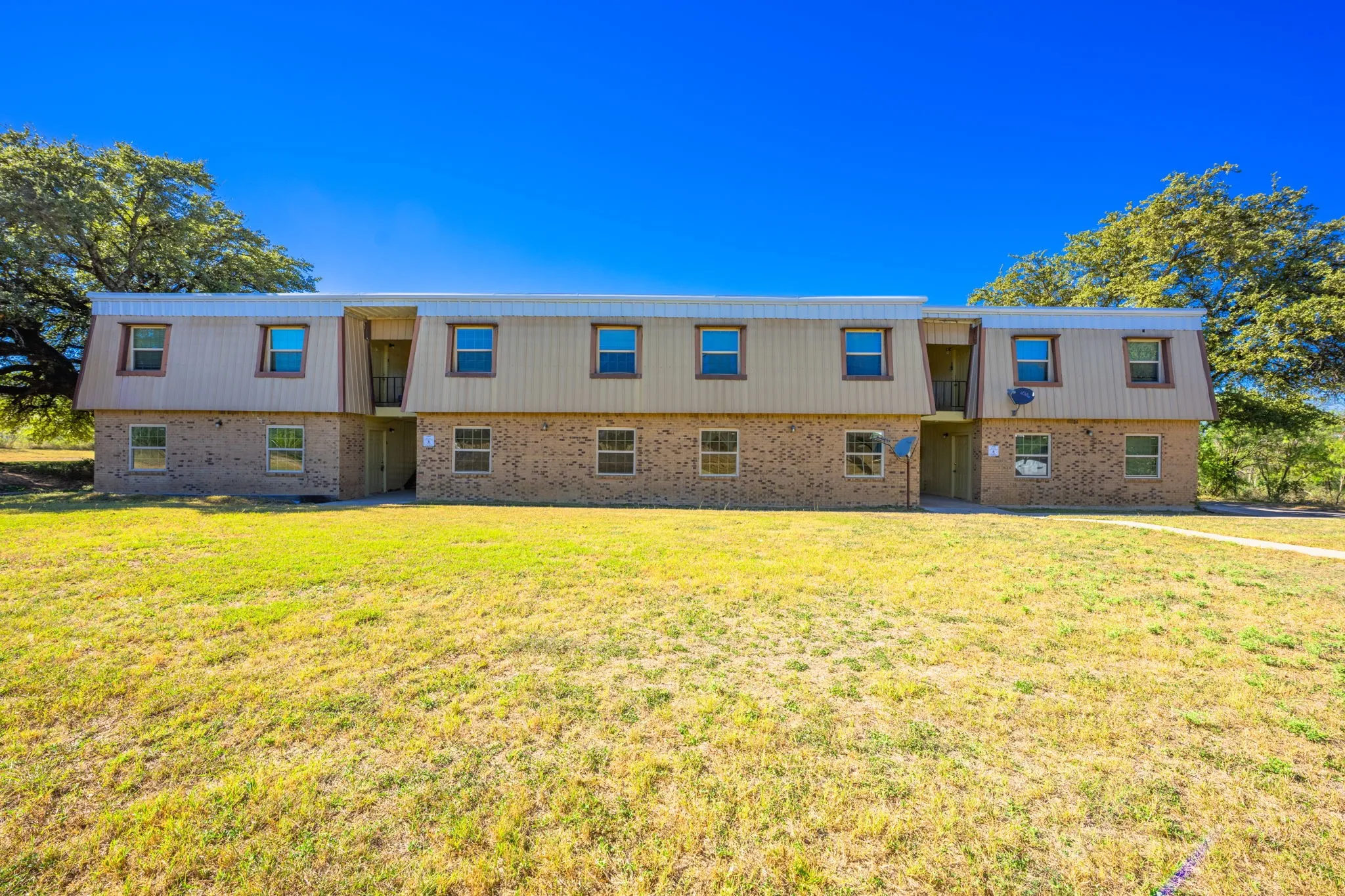 Back of property featuring brick siding, mansard roof, and a yard