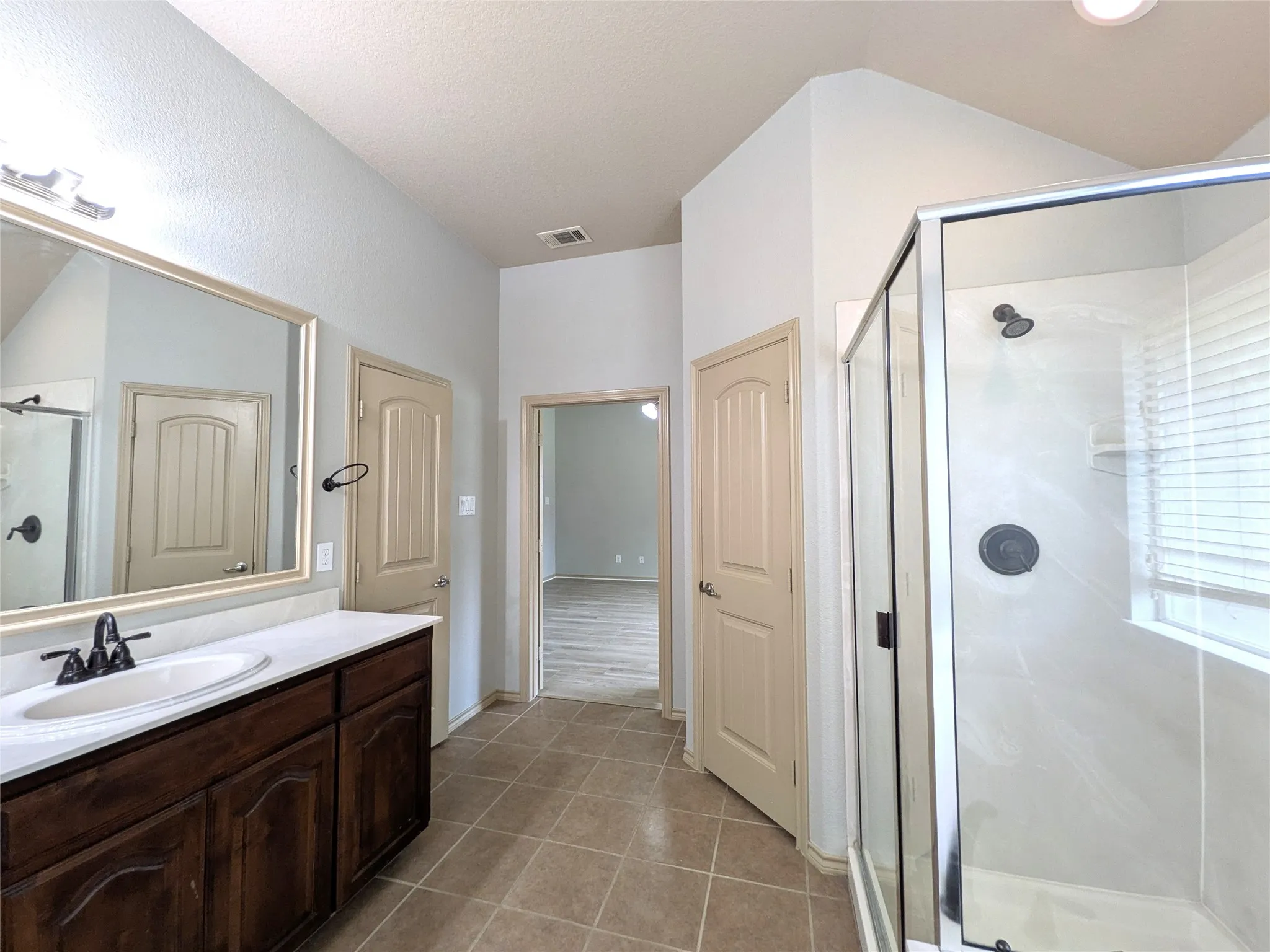 Bathroom featuring a dark wood vanity with a white countertop and integrated sink, a large framed mirror, and a glass-enclosed shower with dark fixtures