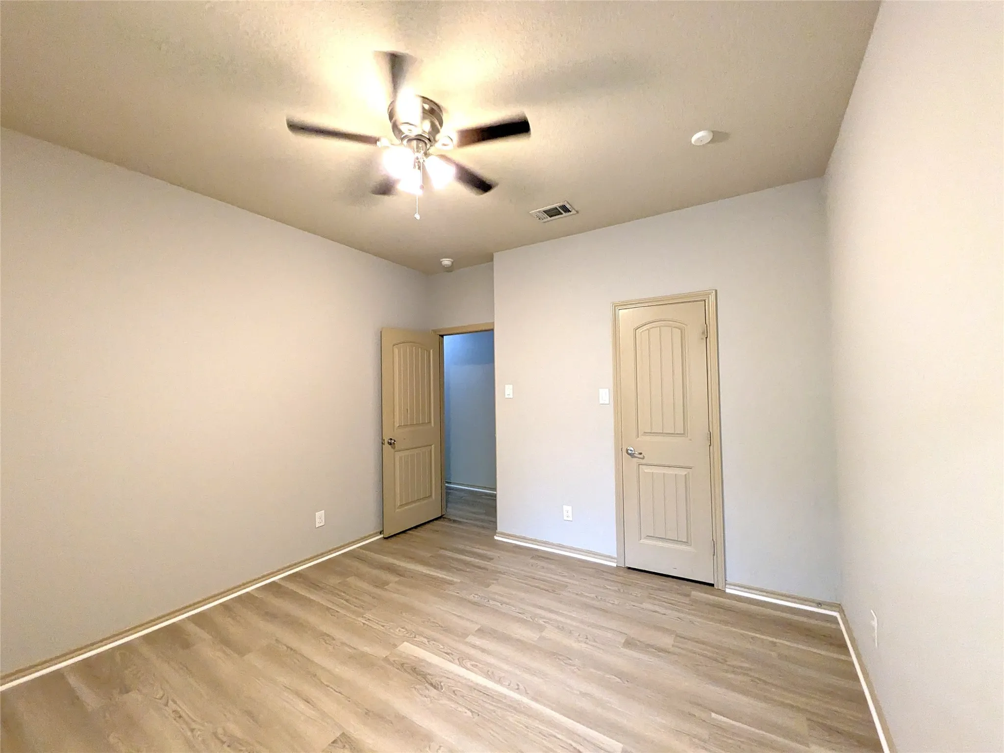 Spacious room featuring wood-finish flooring, neutral-toned walls, and a ceiling fan with integrated lighting