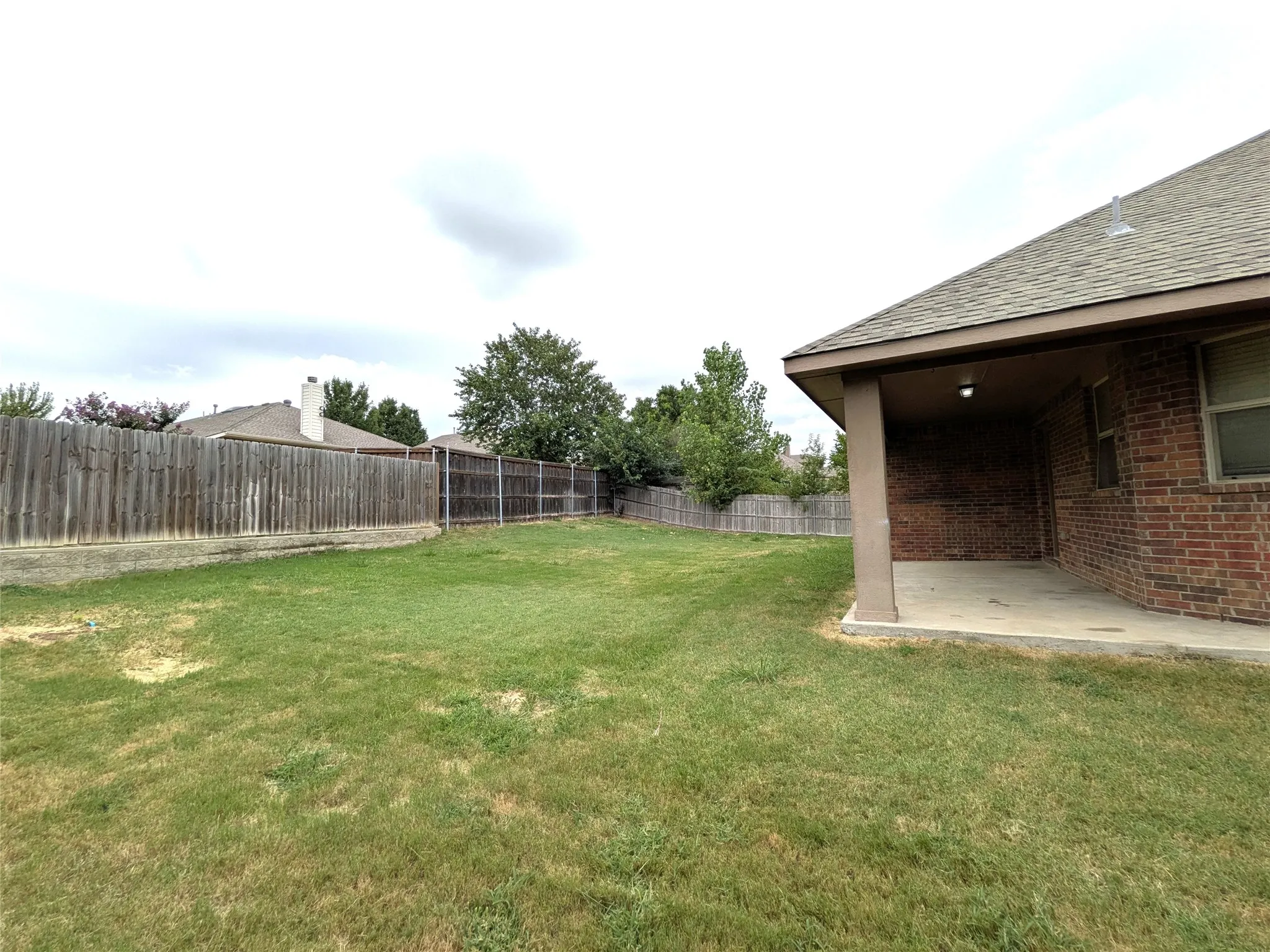 Spacious backyard featuring a covered patio with a concrete slab, a full wood privacy fence, and mature trees