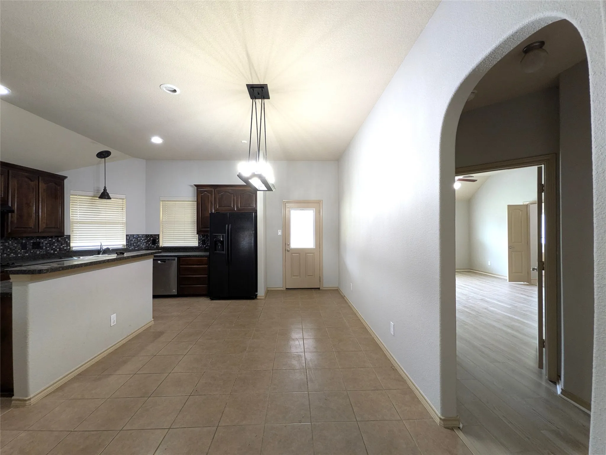 Kitchen and dining area featuring tile flooring, dark wood cabinetry, a solid surface countertop with a mosaic tile backsplash, and stainless steel appliances