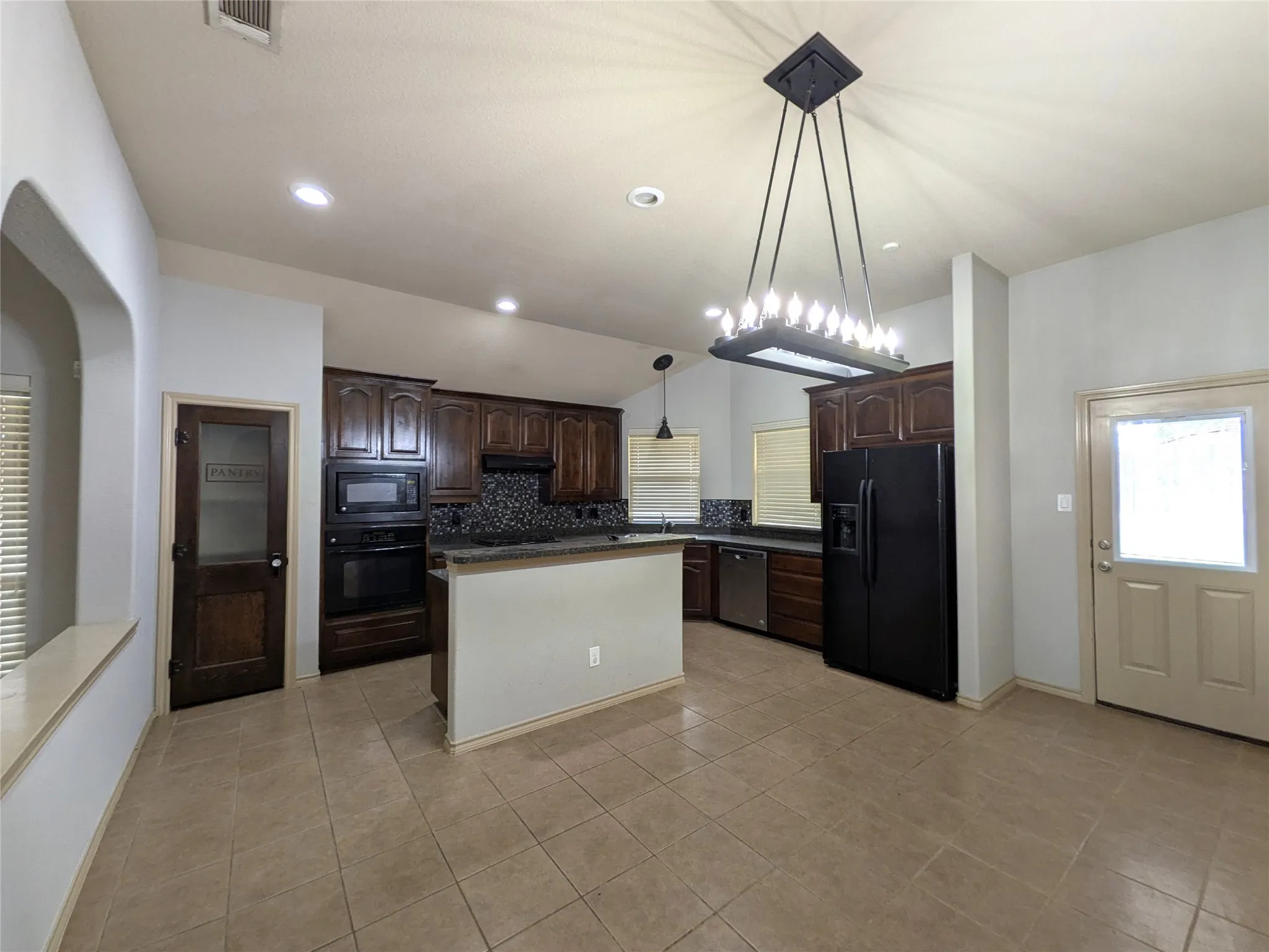 Kitchen with dark wood cabinetry, a mosaic tile backsplash, black appliances, and a central island with a breakfast bar