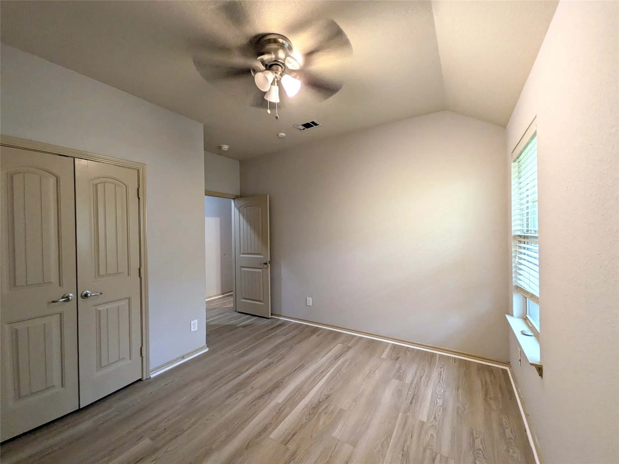 Vaulted ceiling room featuring wood-finish flooring, a ceiling fan with integrated lighting, and a window with horizontal blinds