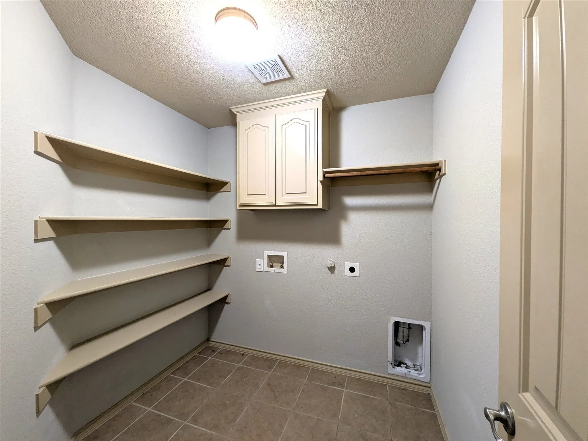 Utility room featuring tile flooring, built-in shelving, overhead cabinetry, and a clothing rod