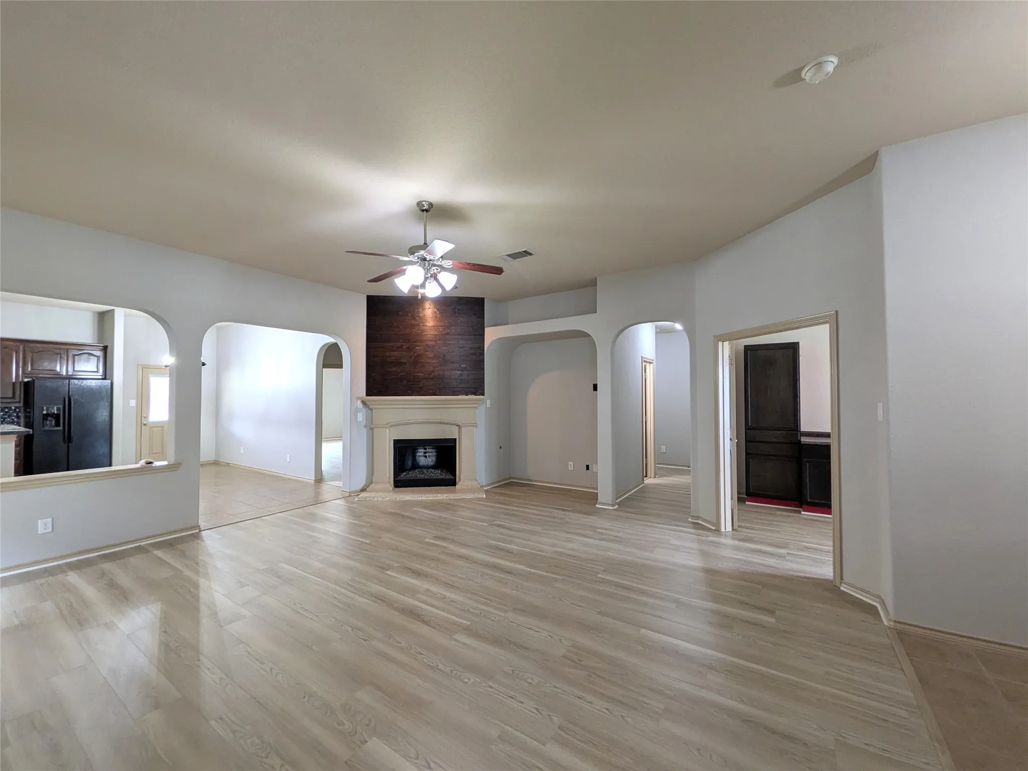 Spacious living area featuring wood-finish flooring, a ceiling fan, and a fireplace with a light-colored mantel and dark-toned accent wall