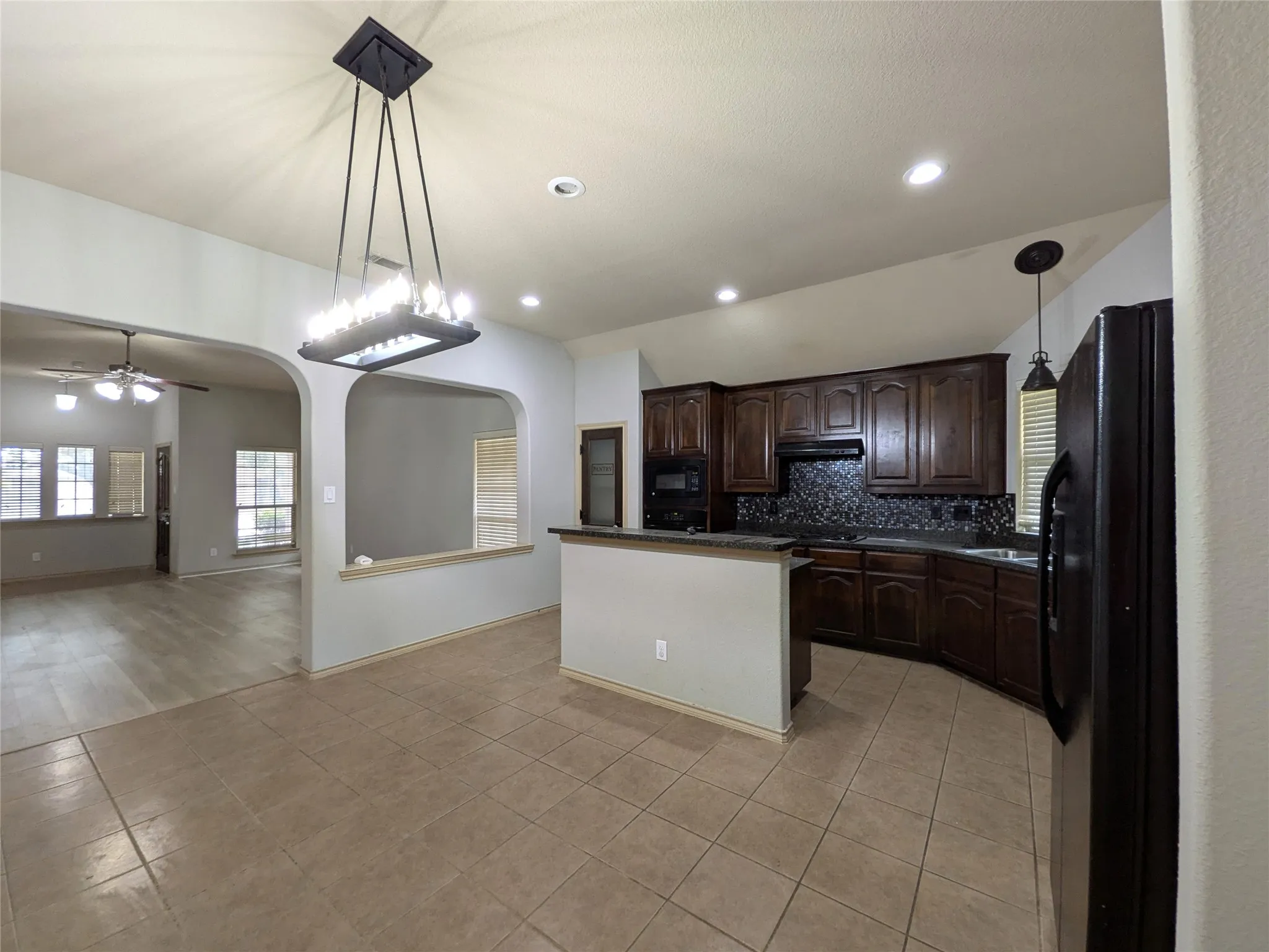 Kitchen with dark wood-finish cabinetry, black appliances, and a tiled backsplash