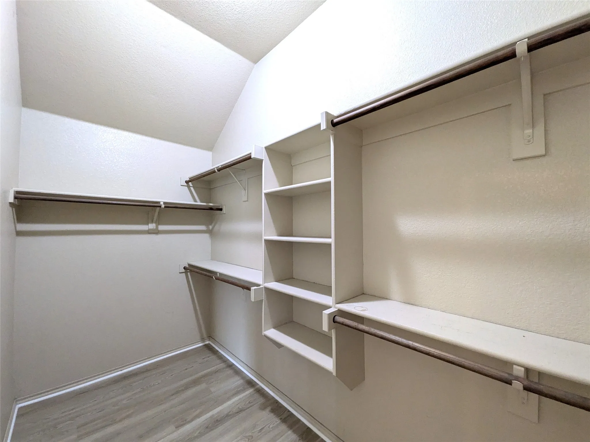 Spacious walk-in closet featuring extensive built-in shelving and multiple garment rods