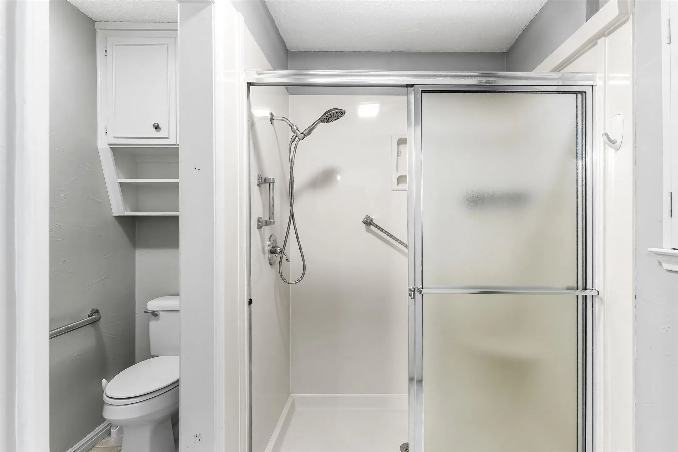 Walk-in shower with frosted glass enclosure, chrome fixtures, and built-in grab bars