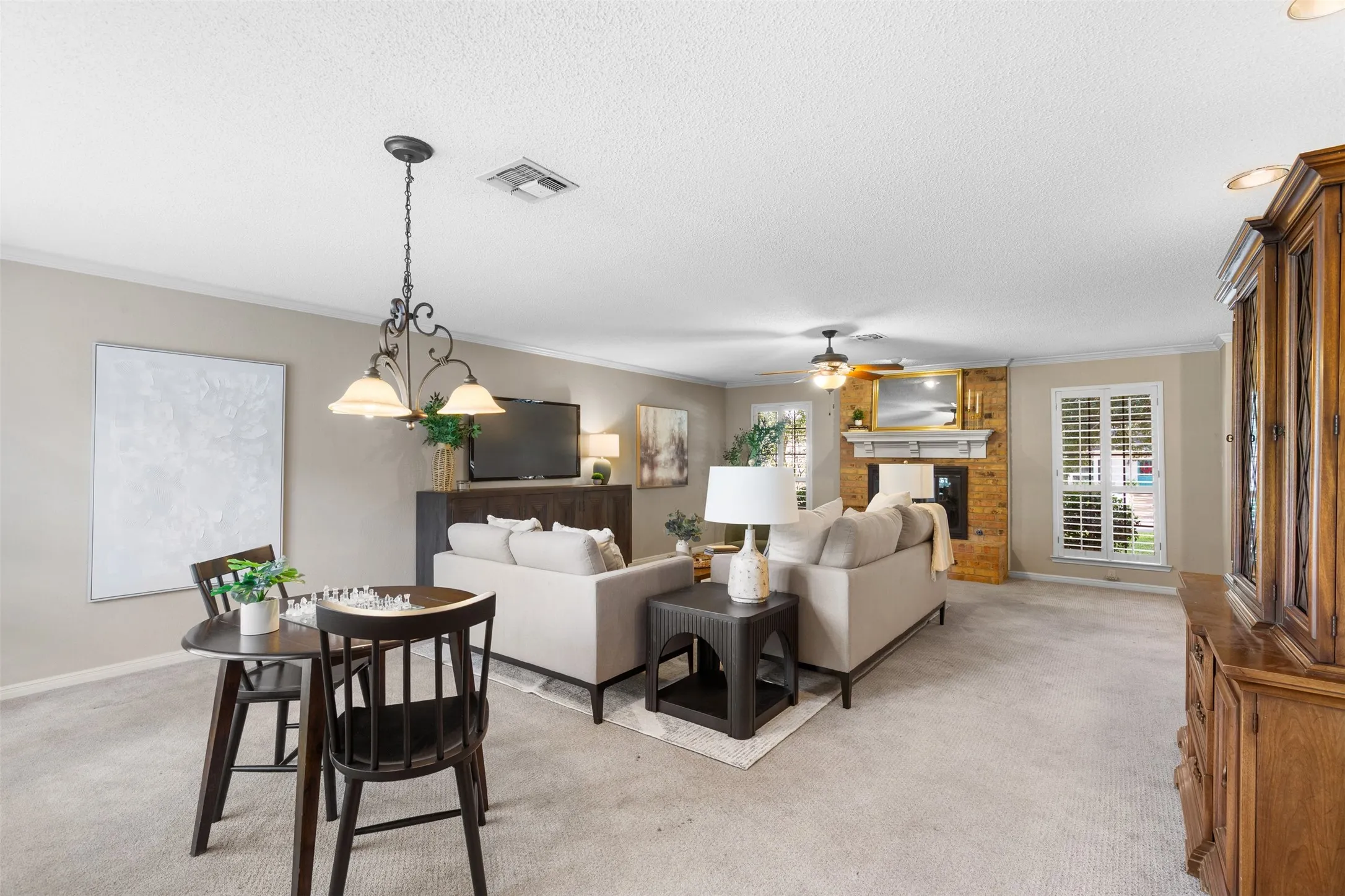 Open-concept living space featuring a stone-clad fireplace, ceiling fan, and plantation shutters