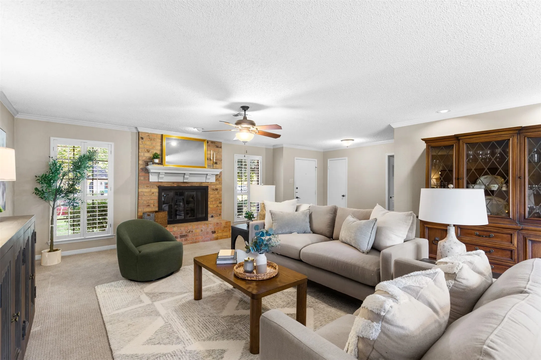 Brick fireplace with a white mantel, ceiling fan, crown molding, recessed lighting, and dual windows with plantation shutters