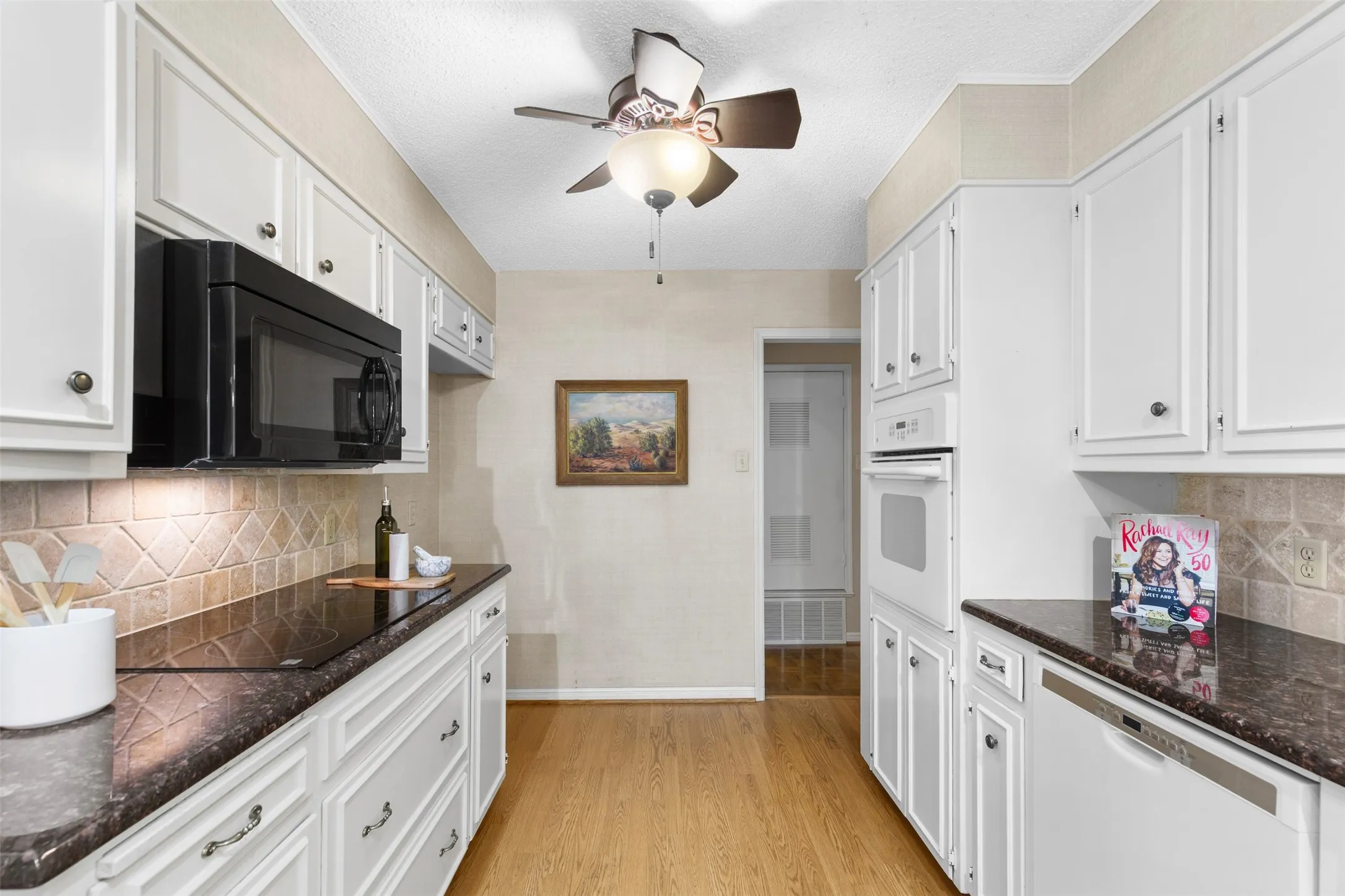 White cabinetry with dark contrasting countertops, tiled backsplash, built-in microwave, and built-in oven