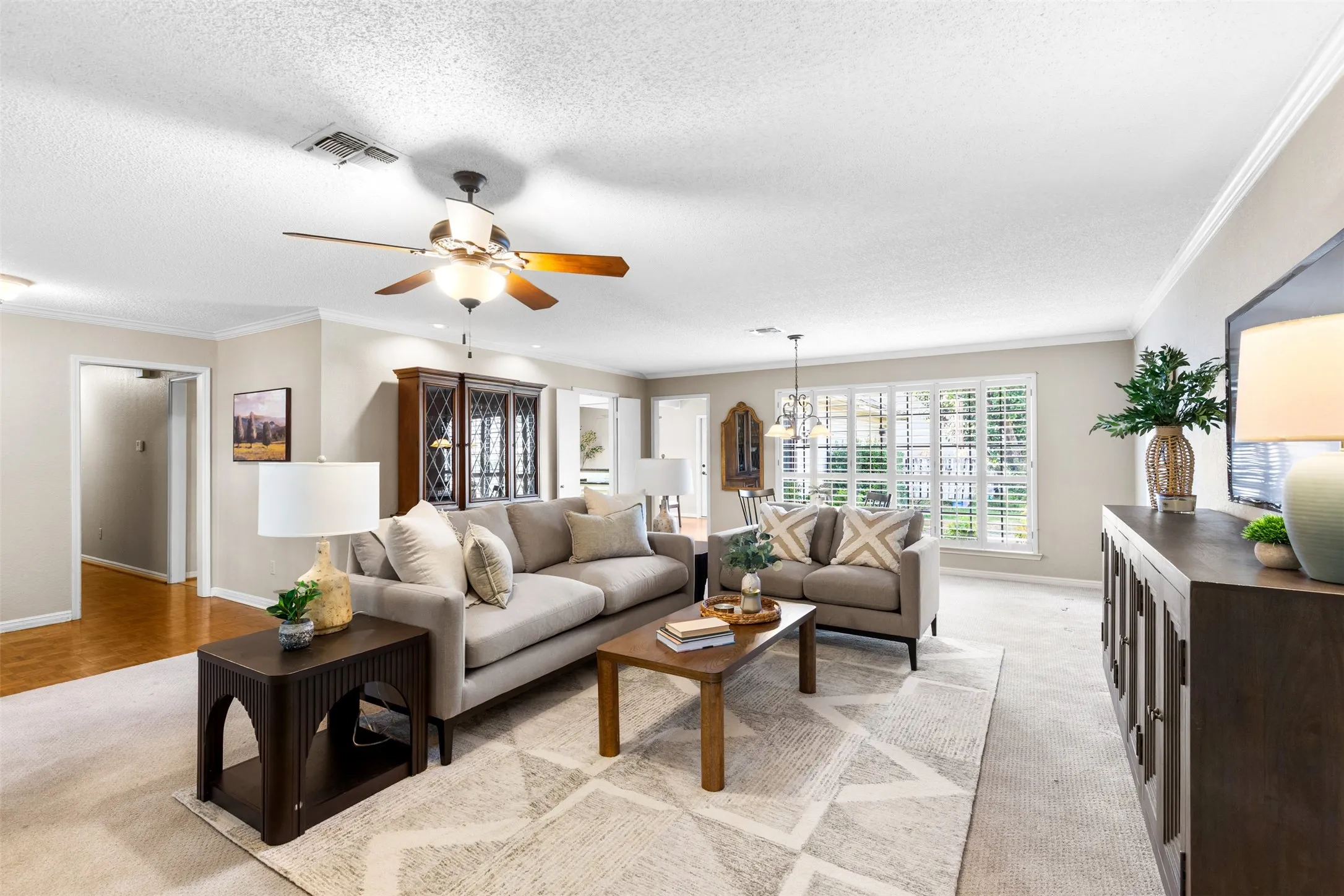 Spacious living area featuring neutral wall tones, crown molding, a ceiling fan fixture, and multiple large windows with plantation shutters