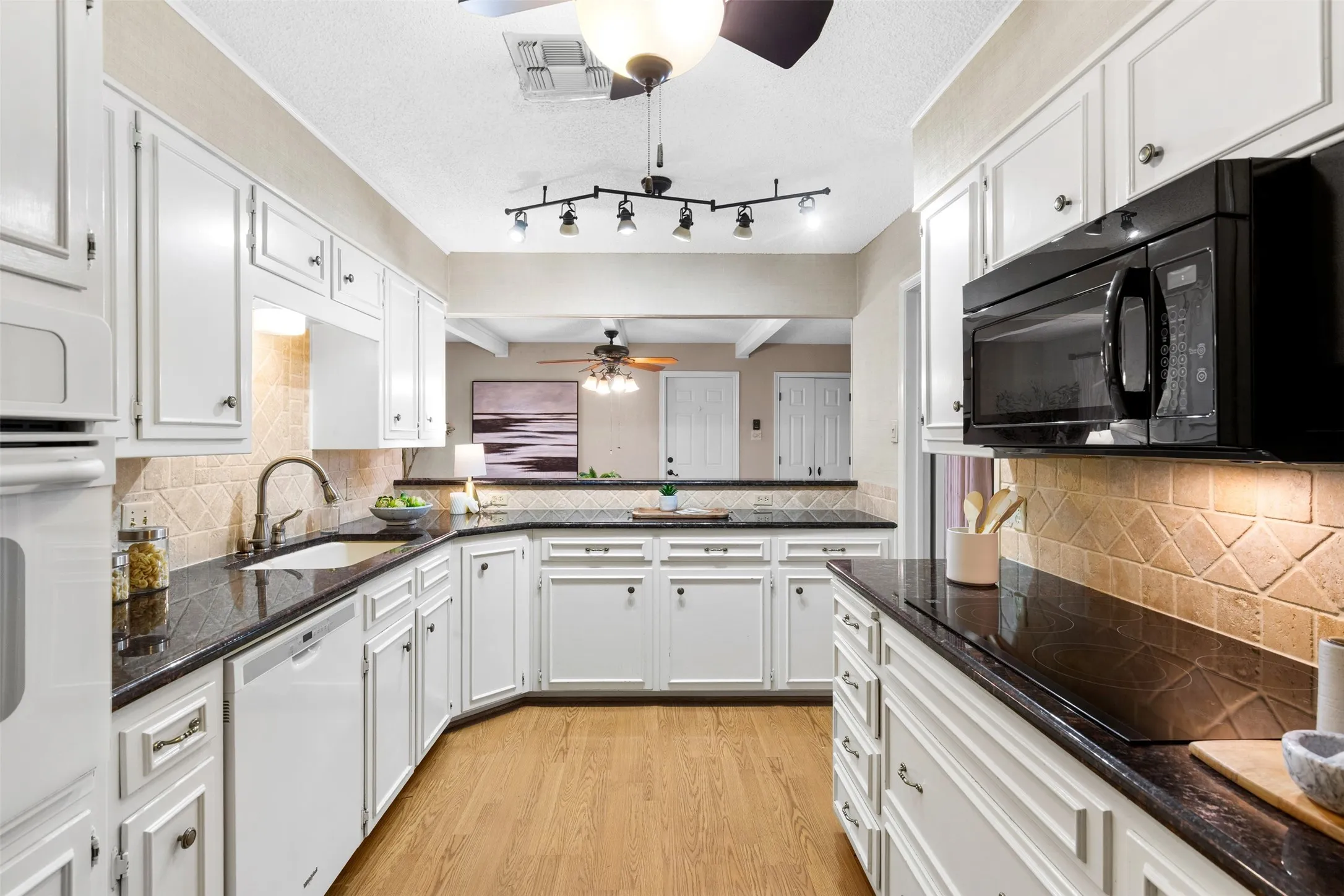 White cabinetry with dark countertops, wood-finish flooring, integrated white appliances, and a tiled backsplash