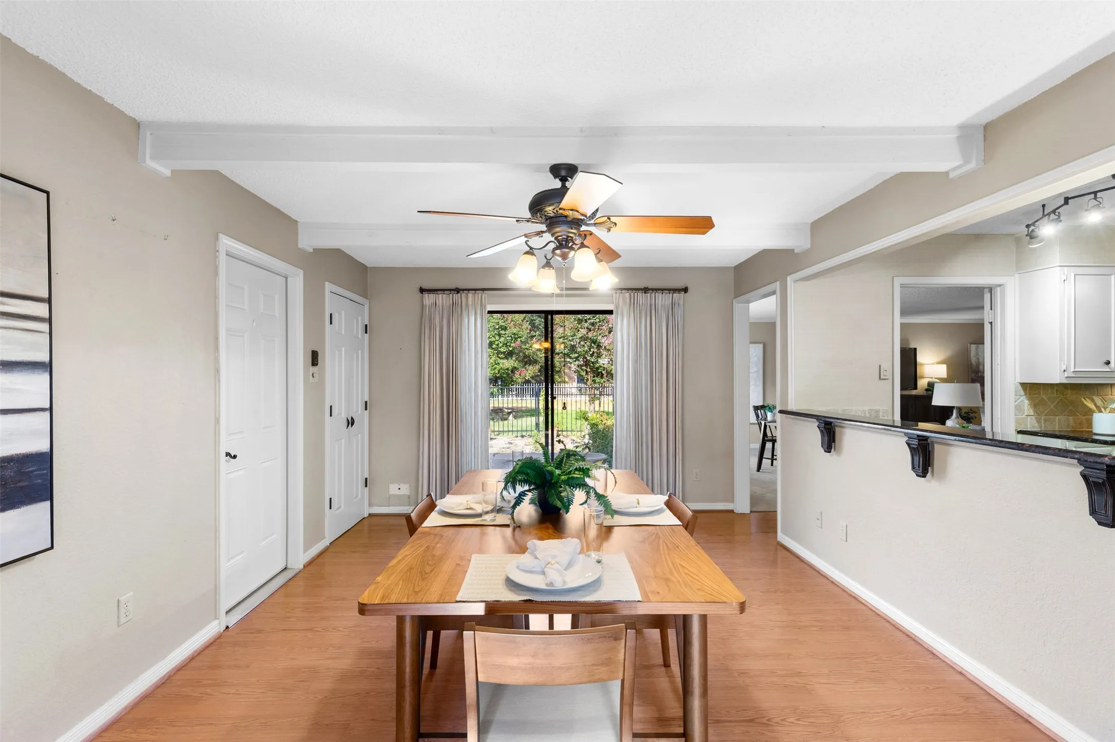 Wood-finish flooring, white ceiling beams, and a decorative ceiling fan
