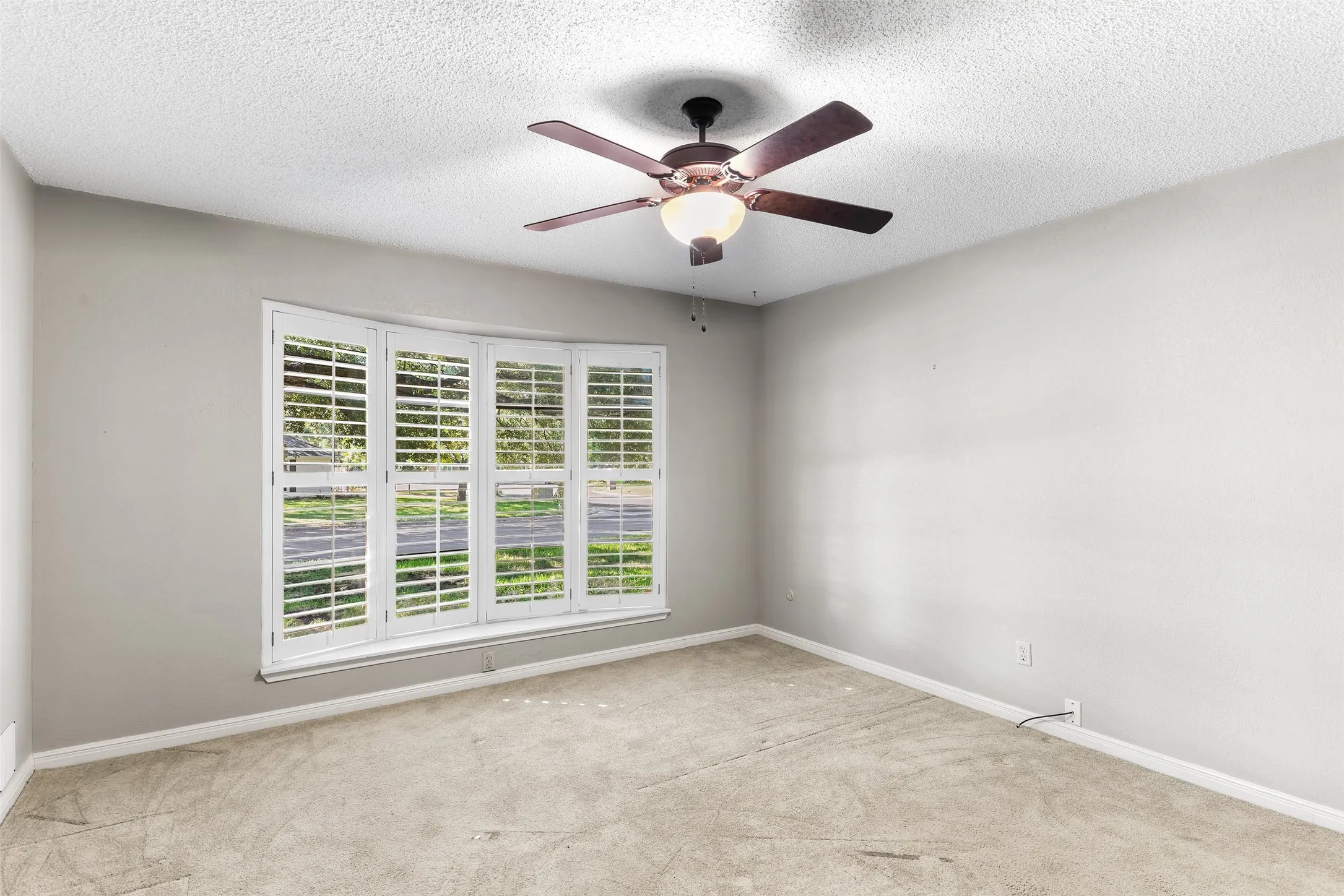 Spacious room featuring a bay window with plantation shutters, a ceiling fan with integrated lighting, and neutral-toned carpeting
